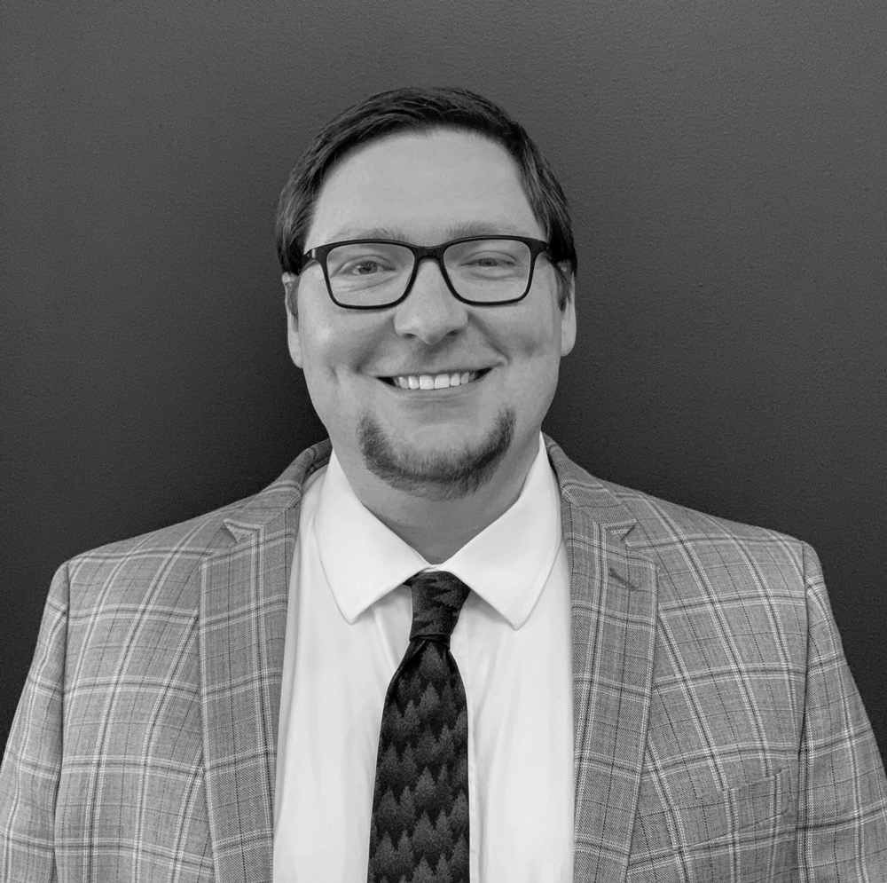 Betz-Scott smiling in a plaid suit and dark tie, black and white image
