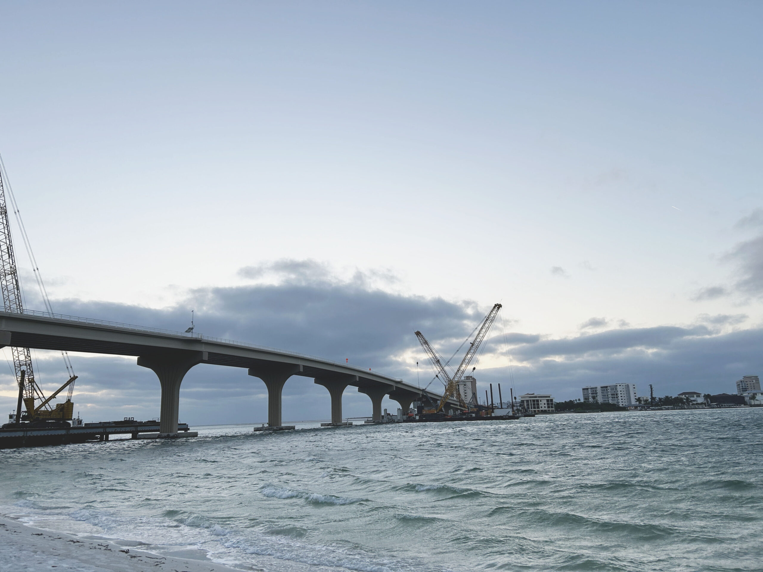 Bridge construction over water with cranes on a cloudy day