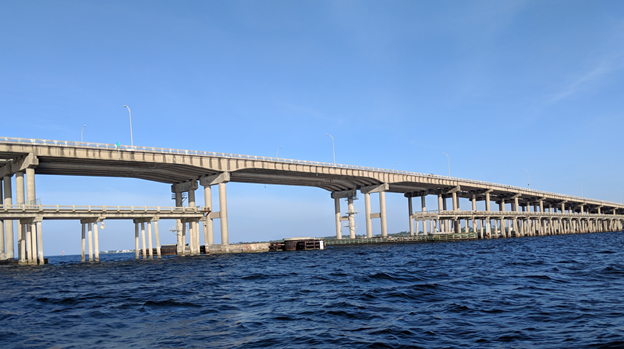 A long concrete bridge stretches over a large body of water under a clear blue sky