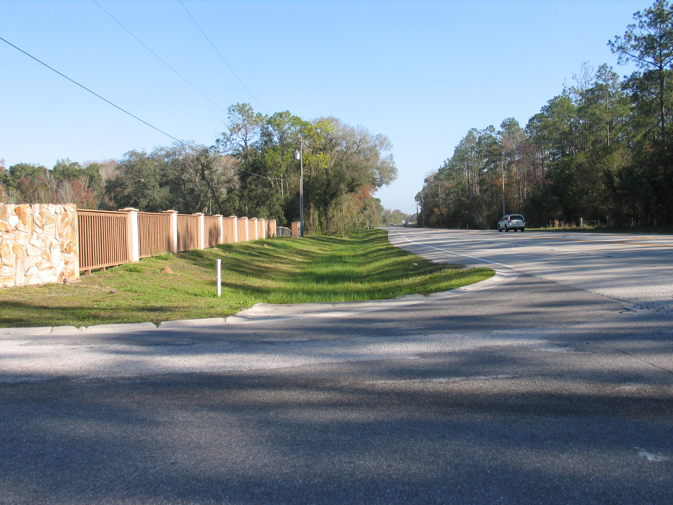 Road with a single car, bordered by a stone wall and trees