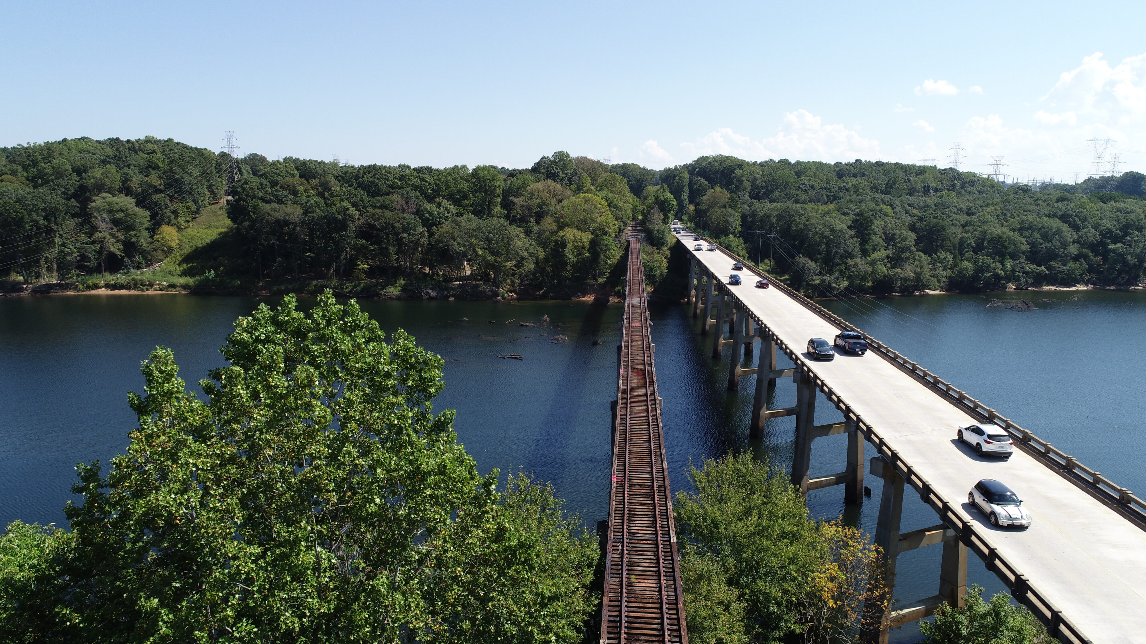 Two parallel bridges over a wide river, surrounded by lush green forest
