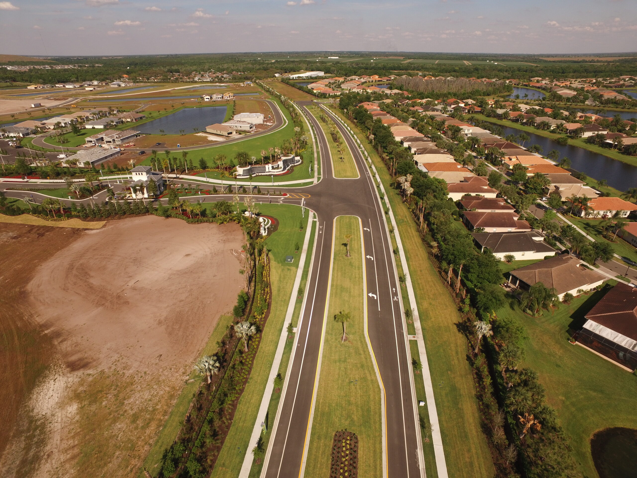 Aerial view of a suburban neighborhood with a large, empty dirt lot, newly paved roads, and houses