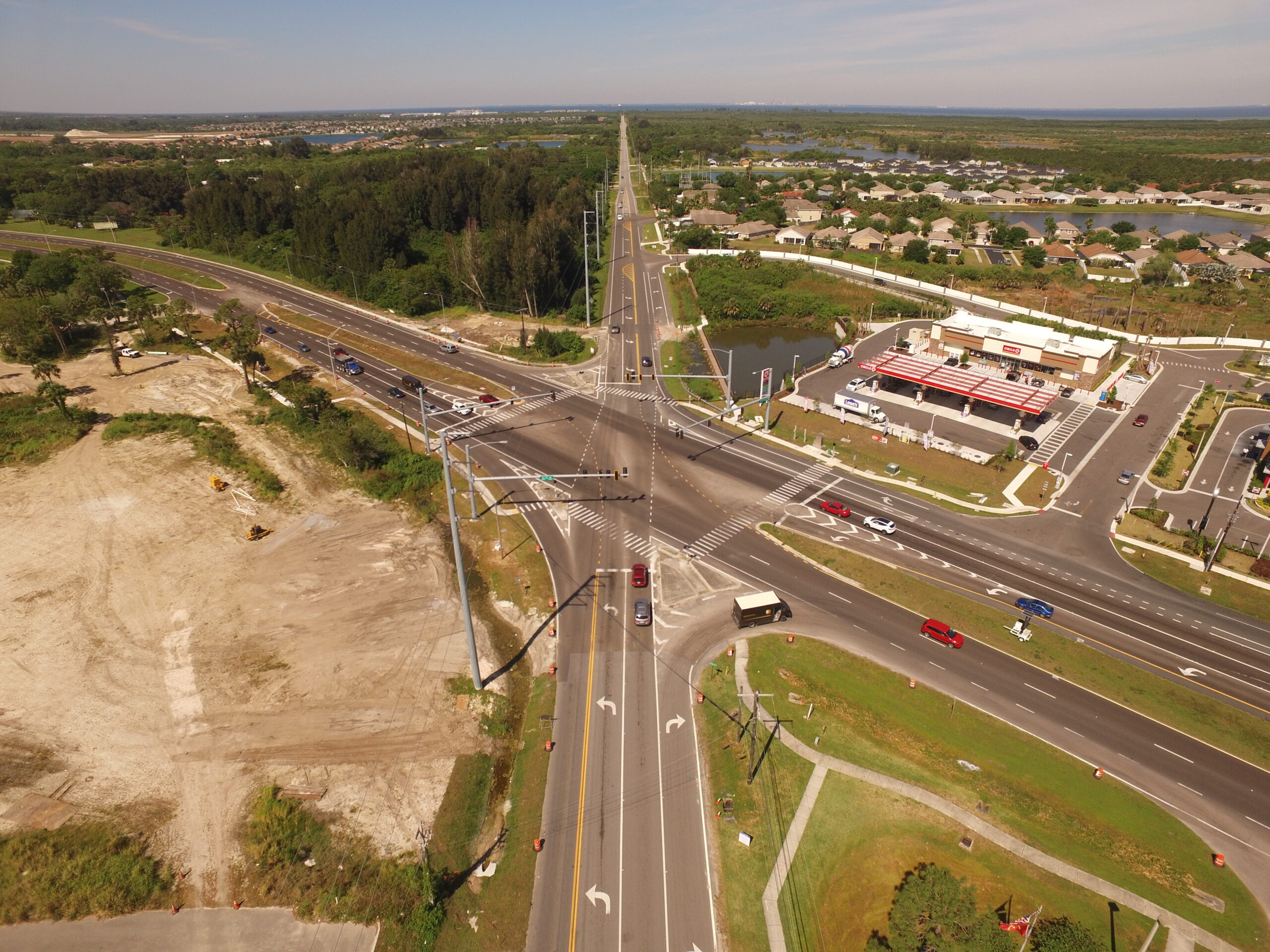 Aerial view of a multi-lane intersection with surrounding greenery, housing, and a gas station