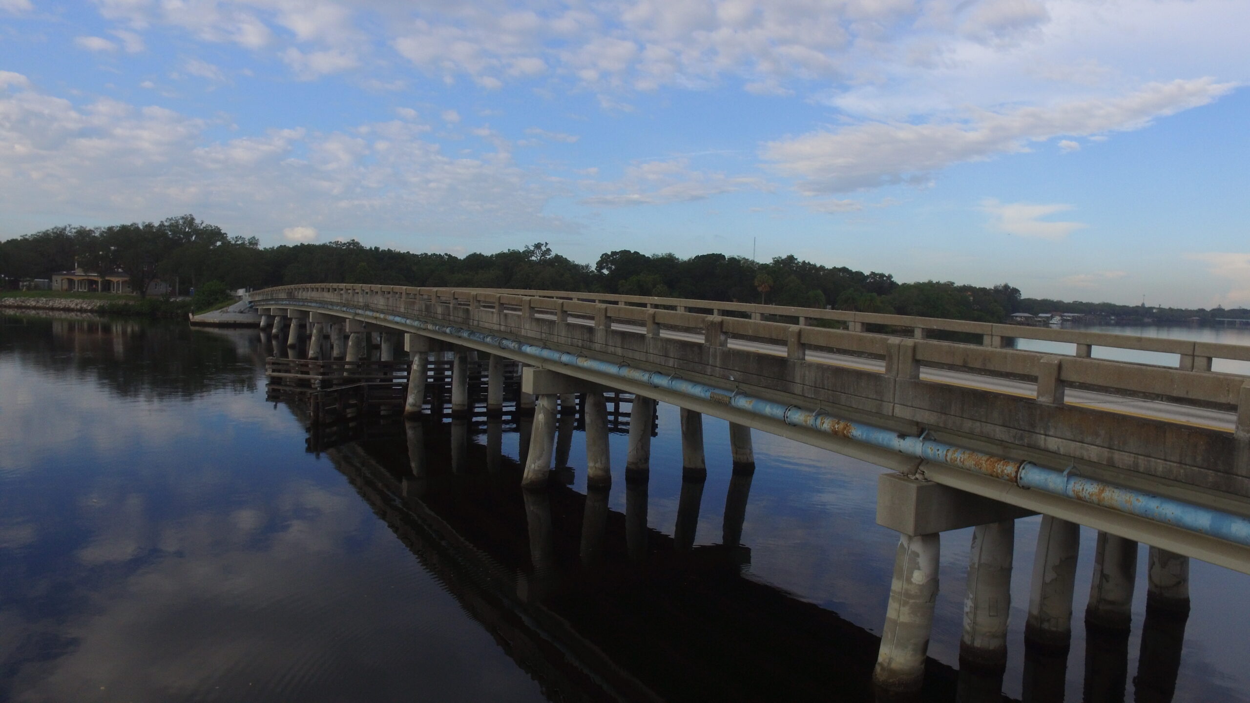 Curved bridge over calm water with partly cloudy sky