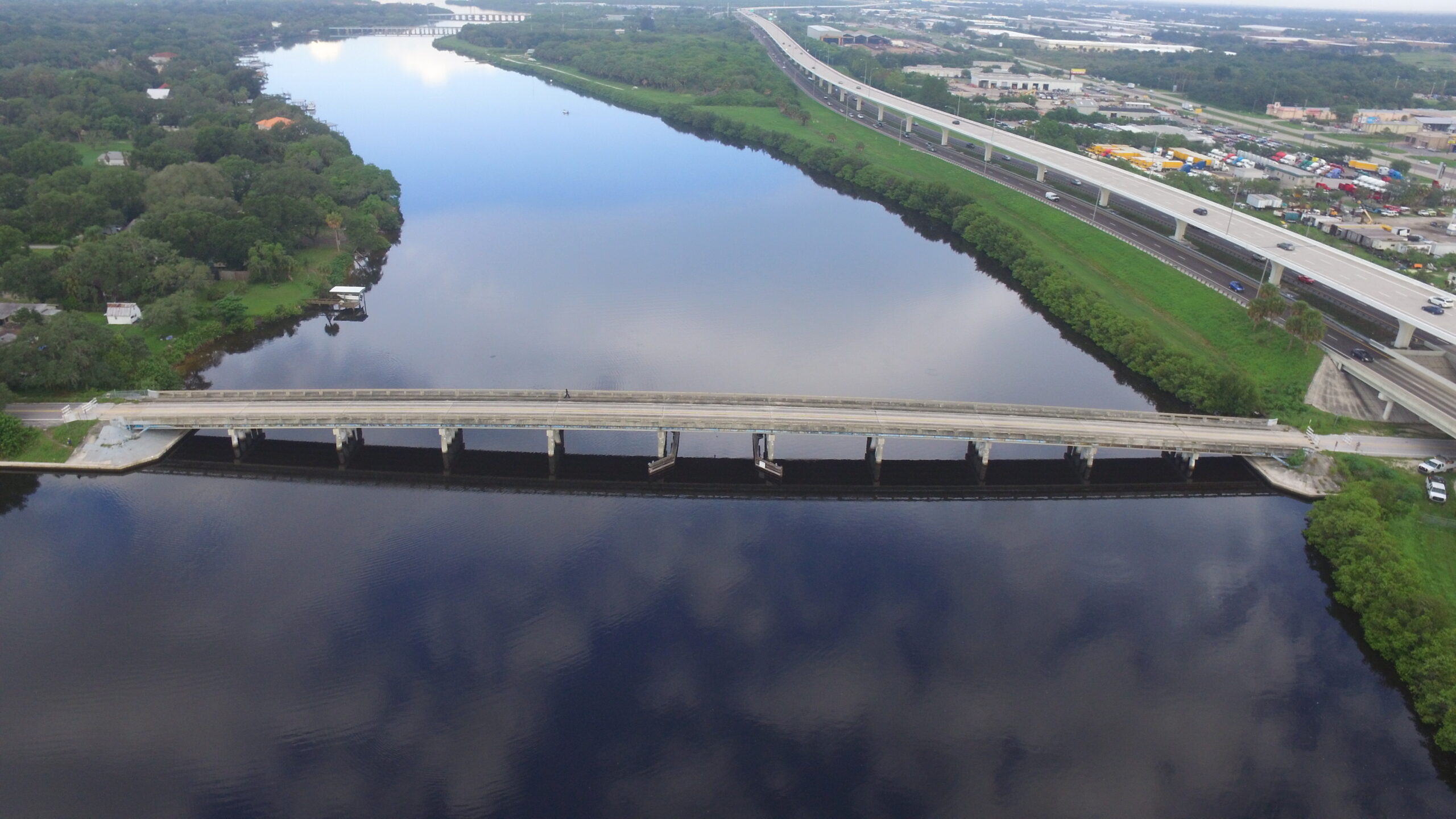 Bridge over a reflective river, flanked by greenery and a nearby highway