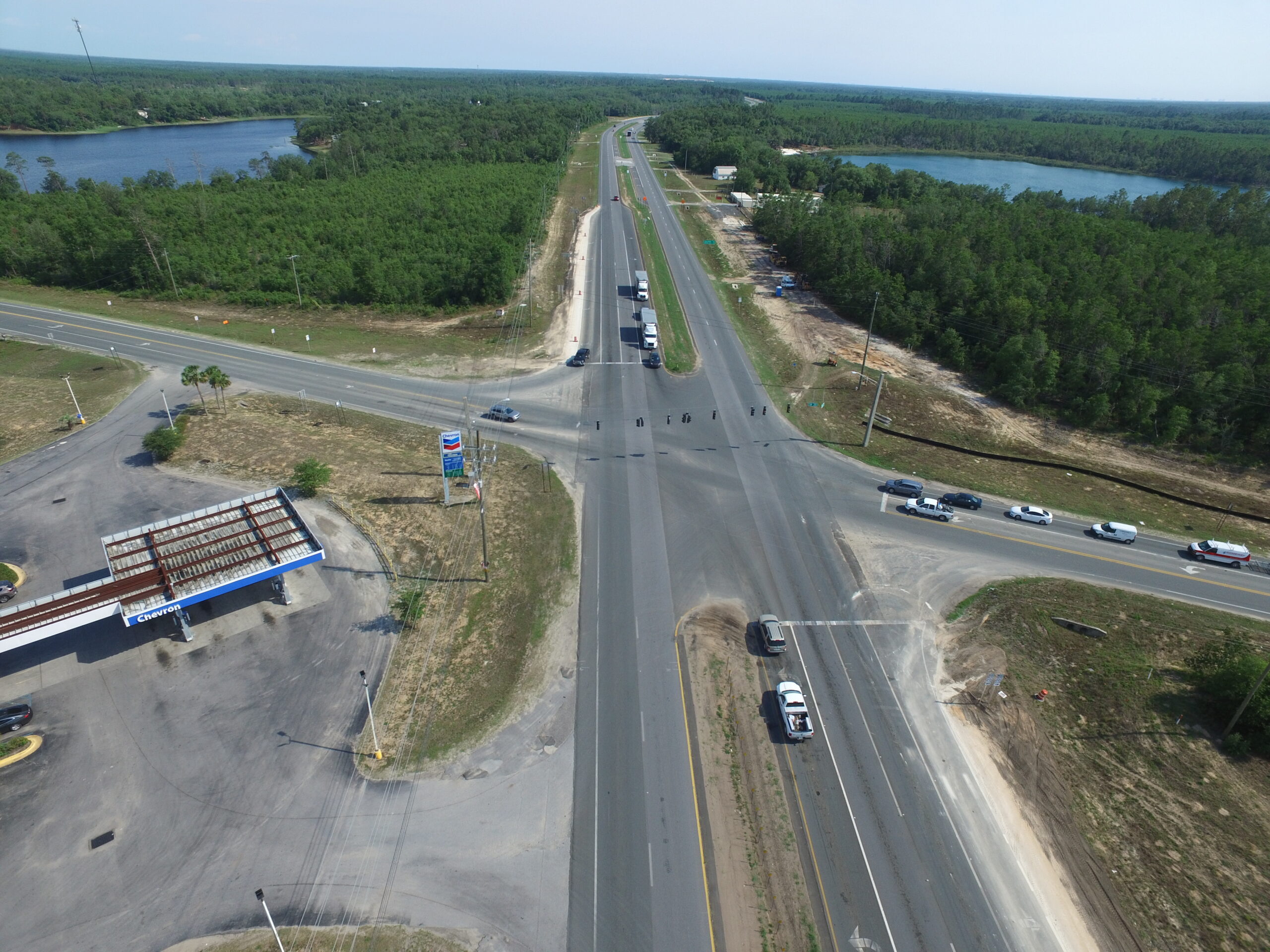 Aerial view of a major highway intersection surrounded by dense forests and lakes. Chevron station visible in the foreground