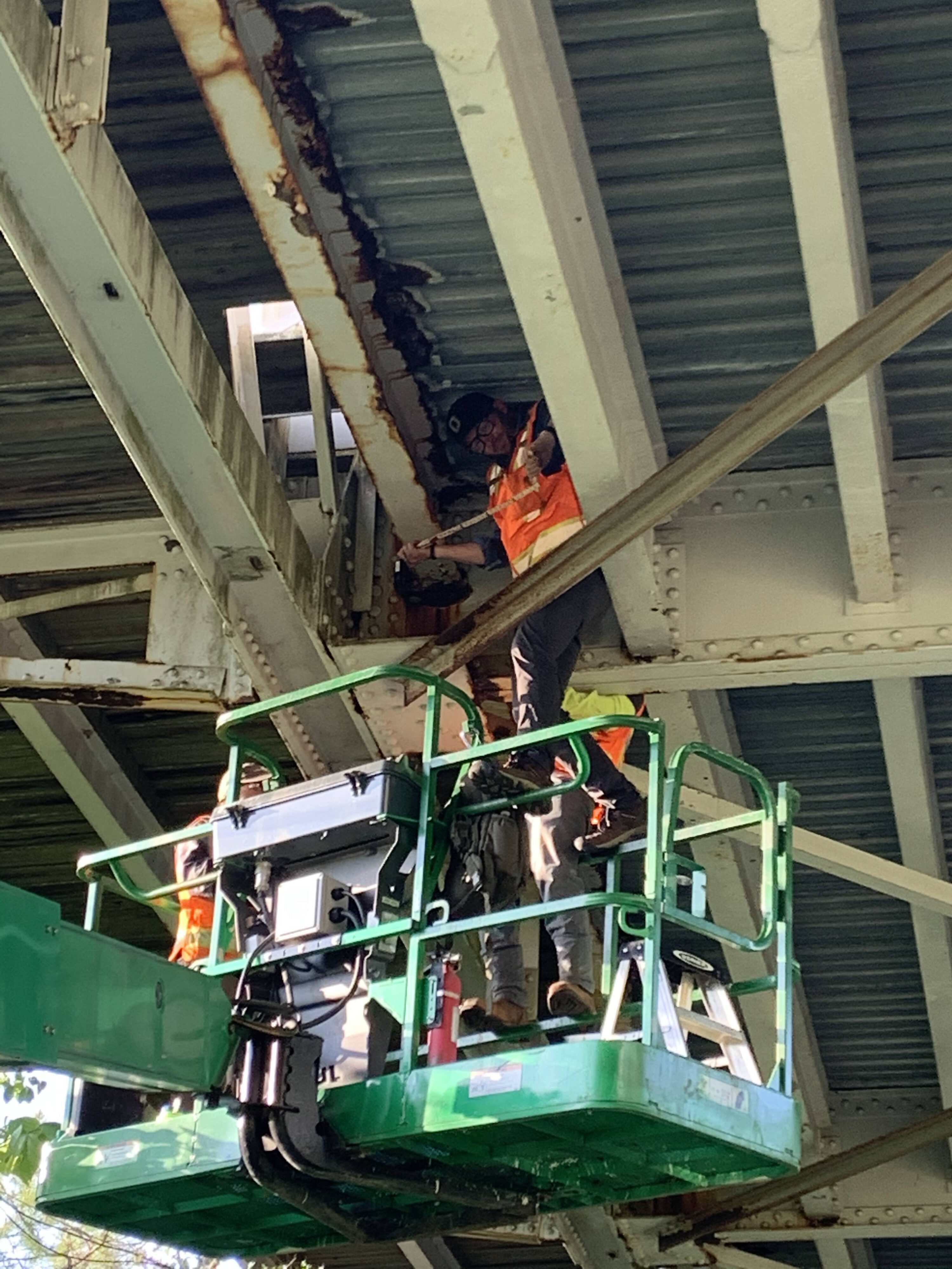 Man in safety gear on green lift inspecting bridge underside
