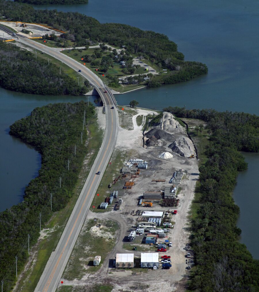Aerial view of Estero Boulevard construction site near a waterway, with sand piles and vehicles