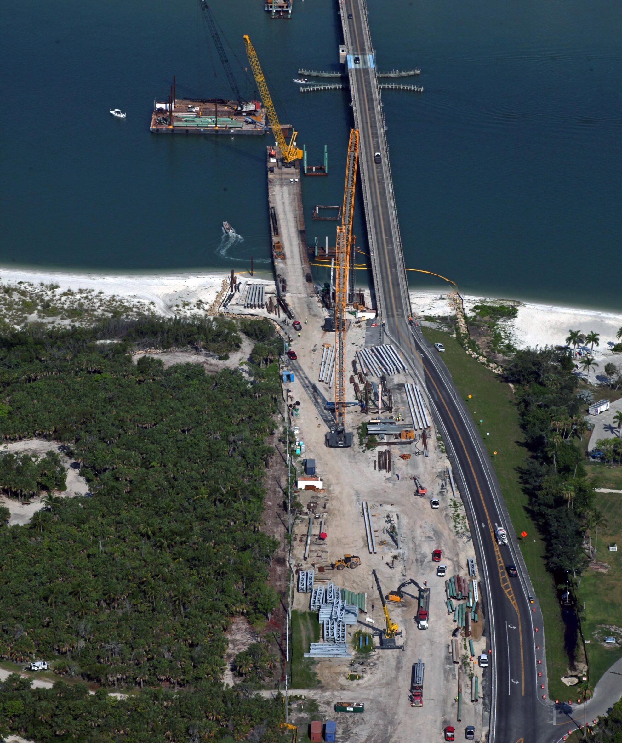 Aerial view of bridge construction with cranes and equipment, connecting land over water. Text: FAST Florida Aerial Services, 1-800-723-7425, @FAST www.FastAerial.com
