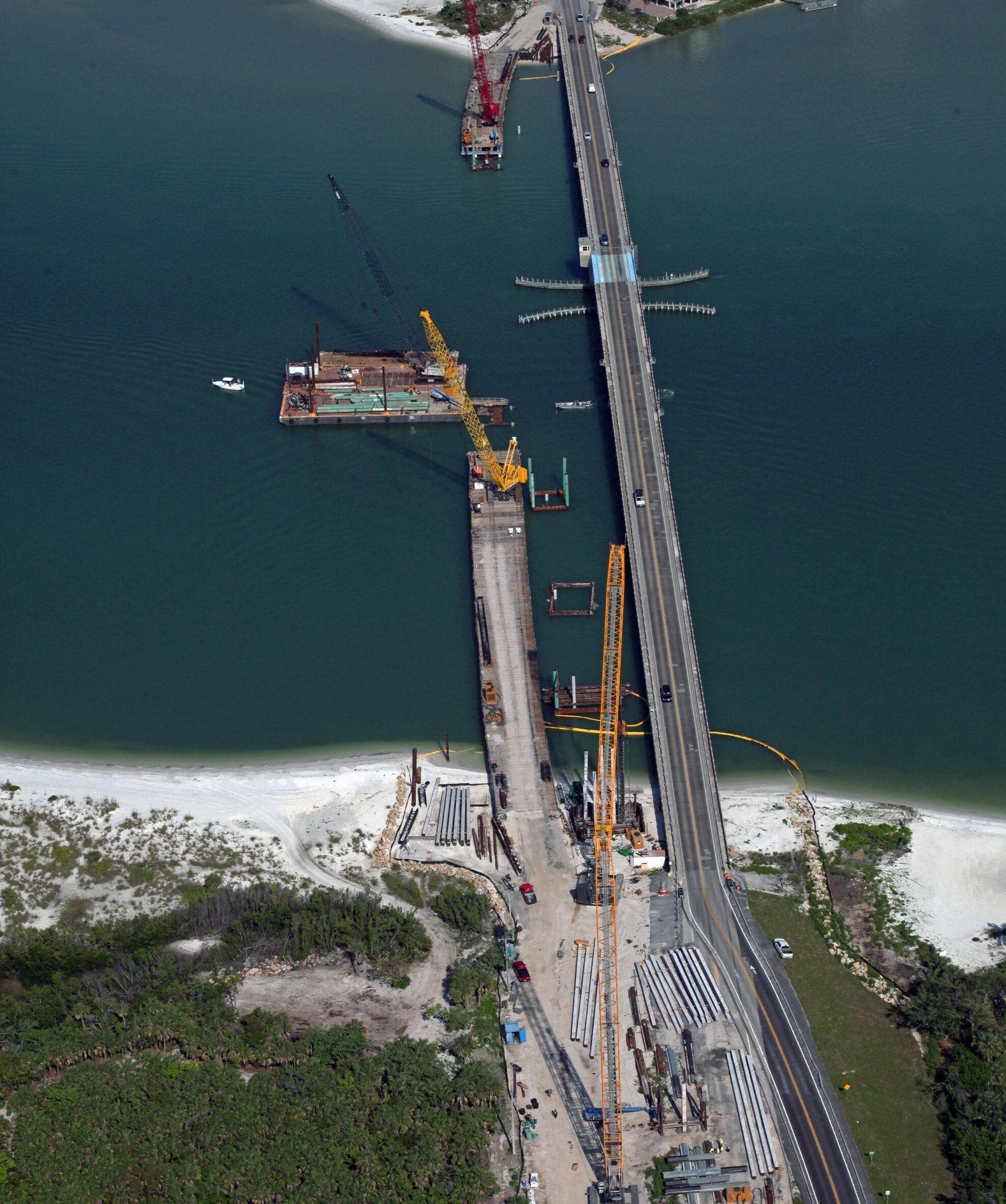 Aerial view of bridge construction with cranes over water, EsteroBlvd scene. FAST logo, contact details in the corner