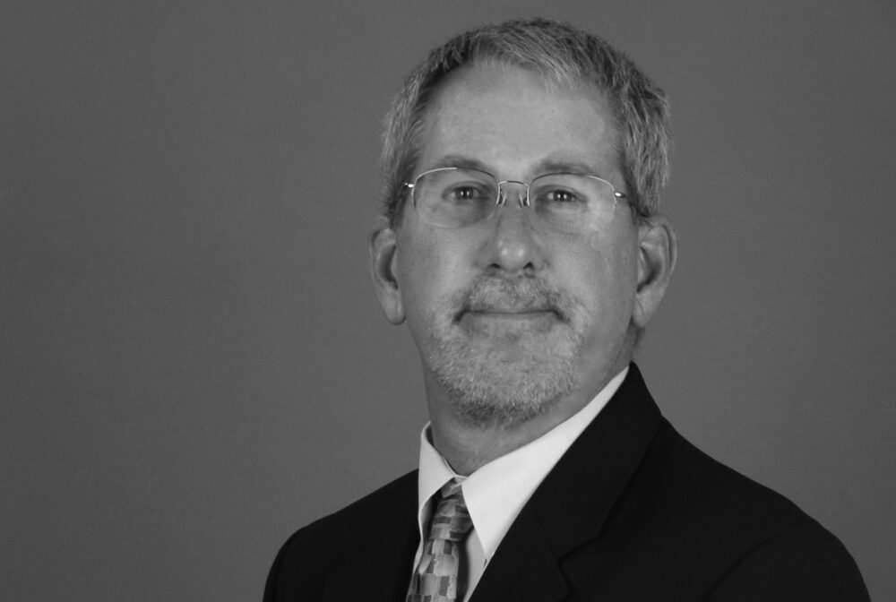 Foley-Paul2 in a suit, neutral expression, gray background