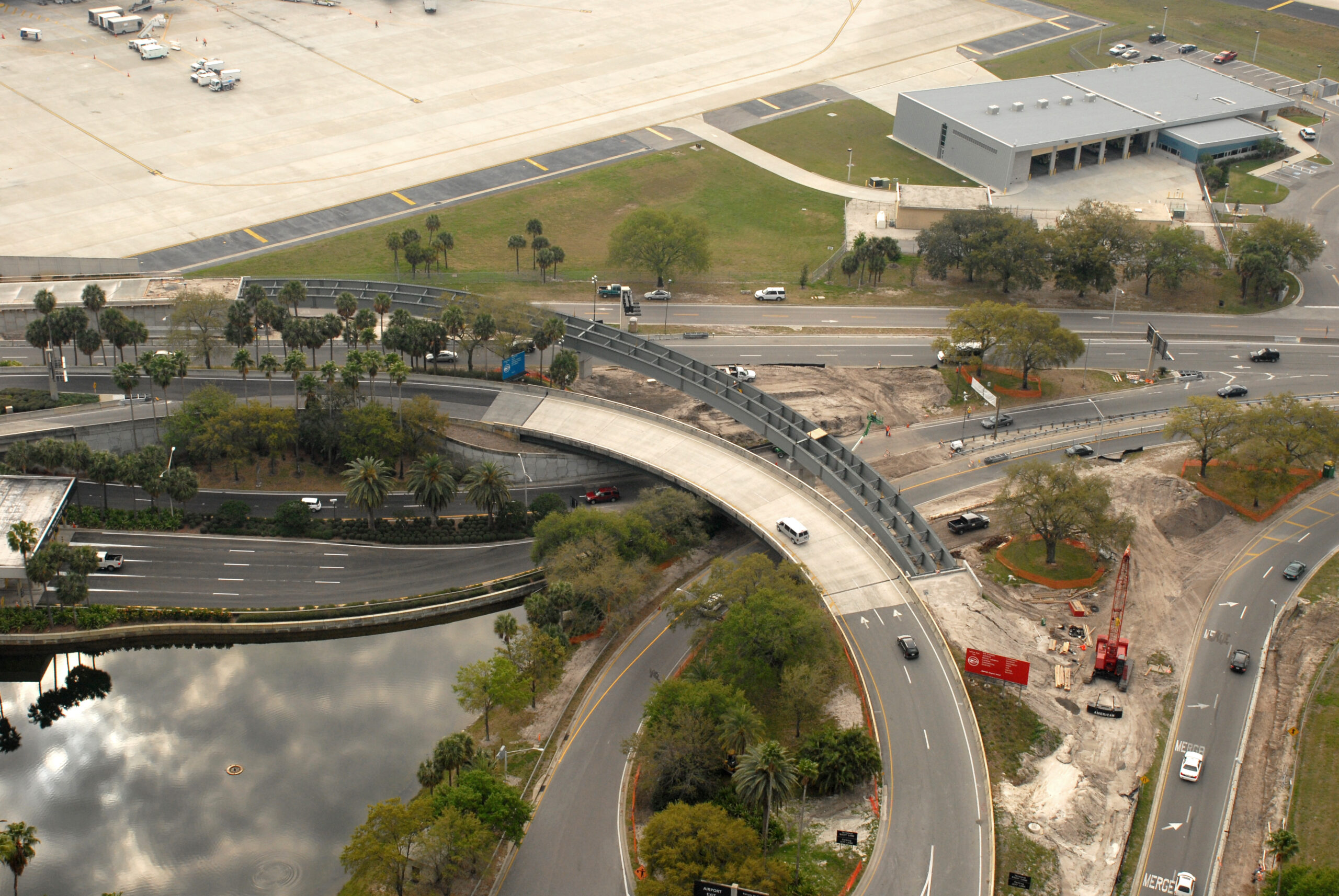 Aerial view of George-Bean-Pkwy construction progress, roads curving, vehicles moving, green spaces, and nearby airport