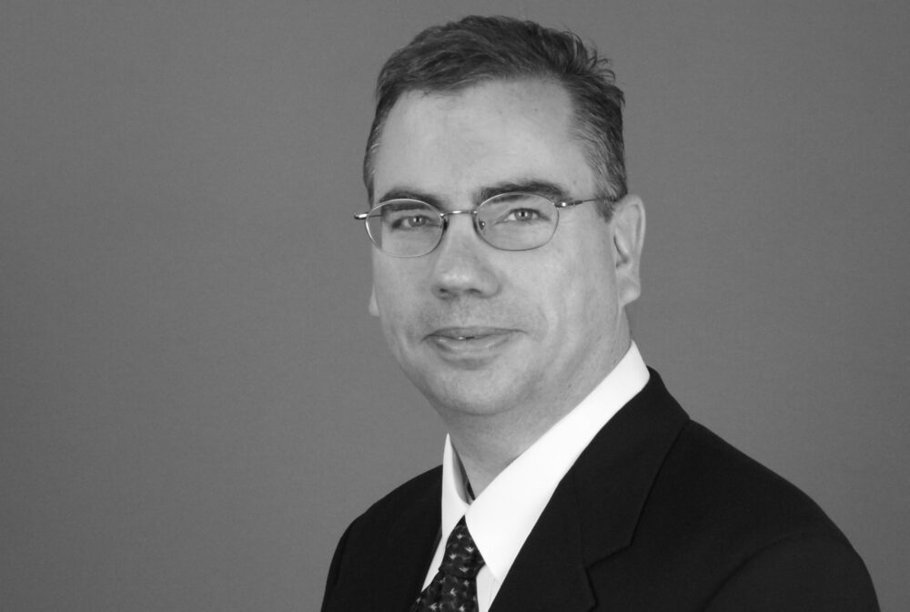 Hubert David smiling in a suit and tie, black-and-white portrait