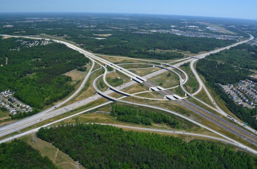 Aerial view of complex highway interchange surrounded by green forest and residential areas