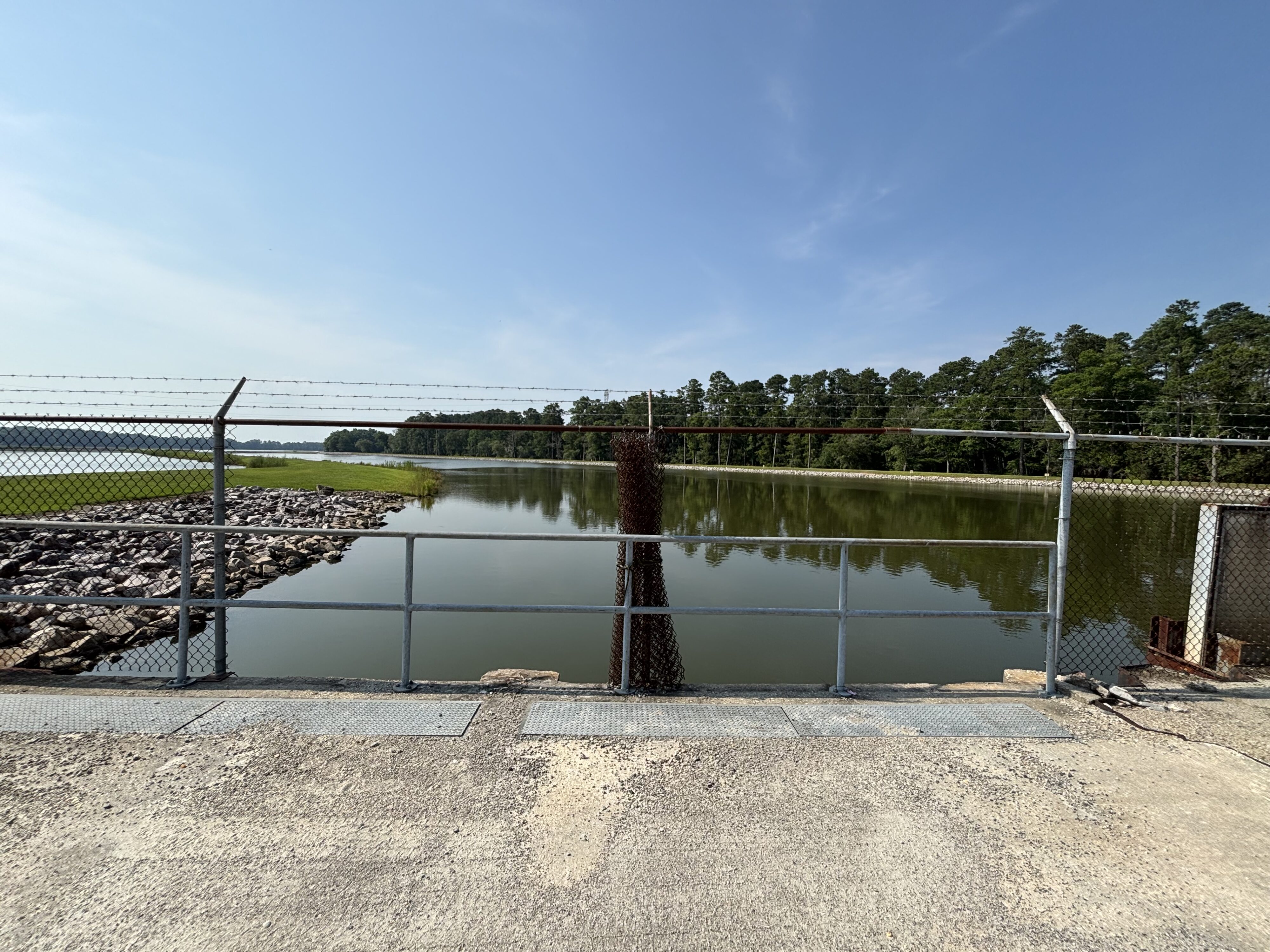 Fenced lake view with surrounding trees and rocky shoreline under clear sky