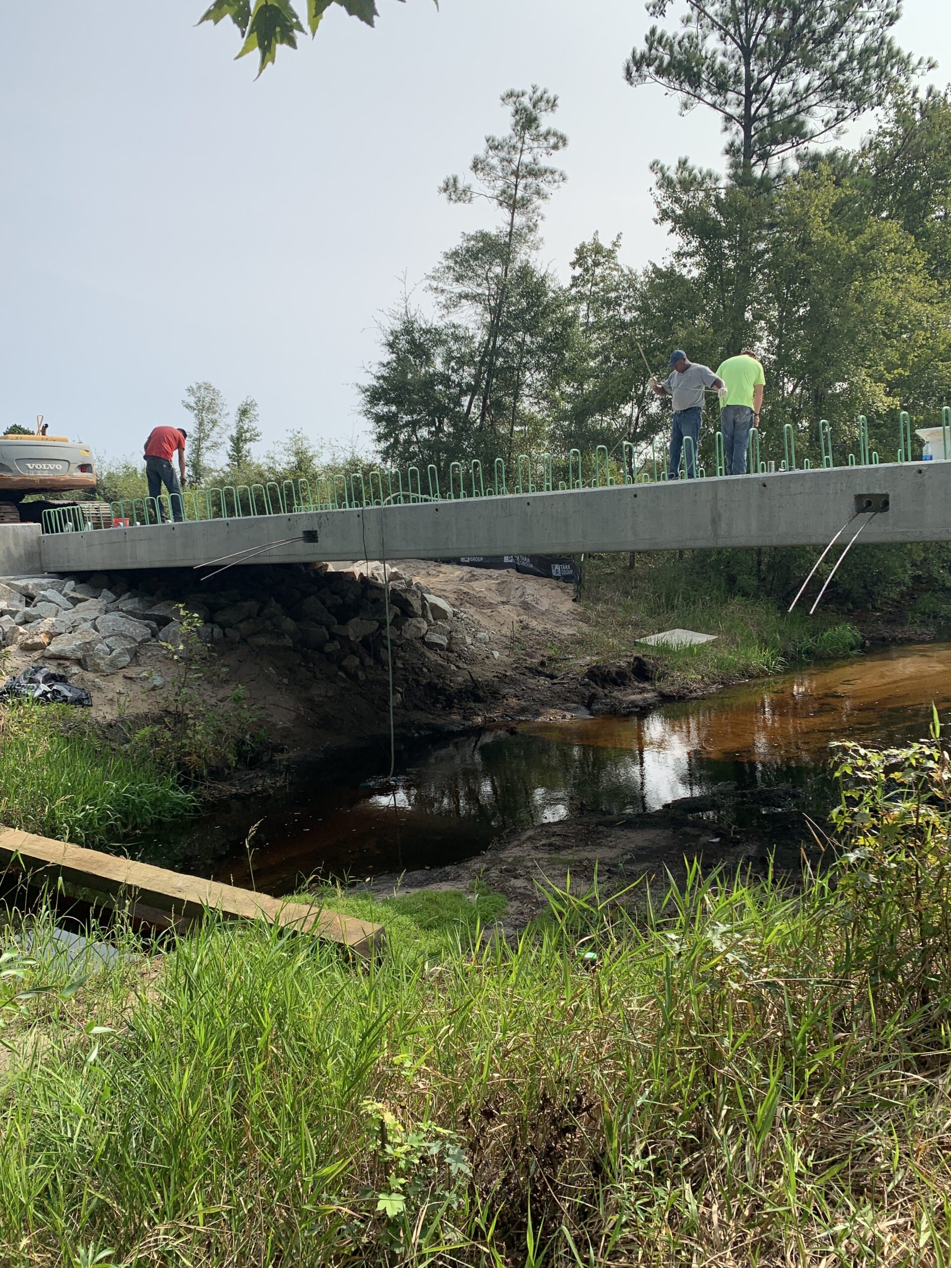 Three construction workers on a bridge over a creek, surrounded by trees