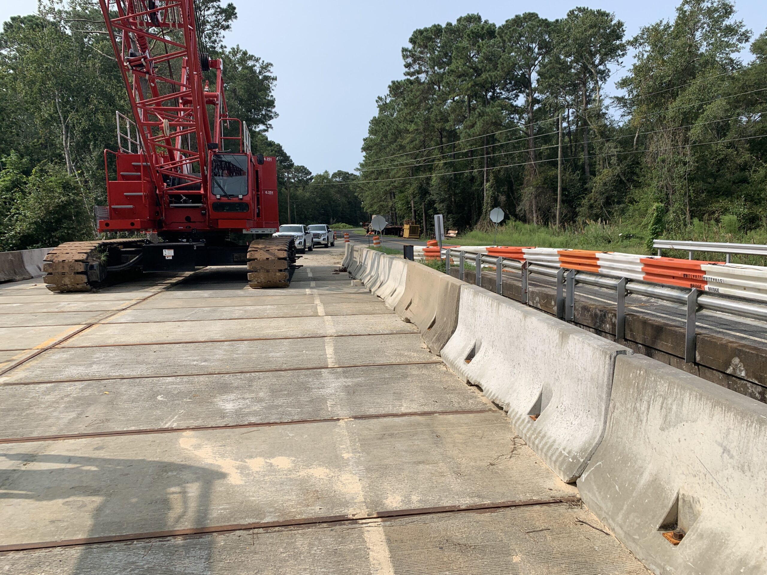Red construction crane on a bridge with concrete barriers and surrounding forested area