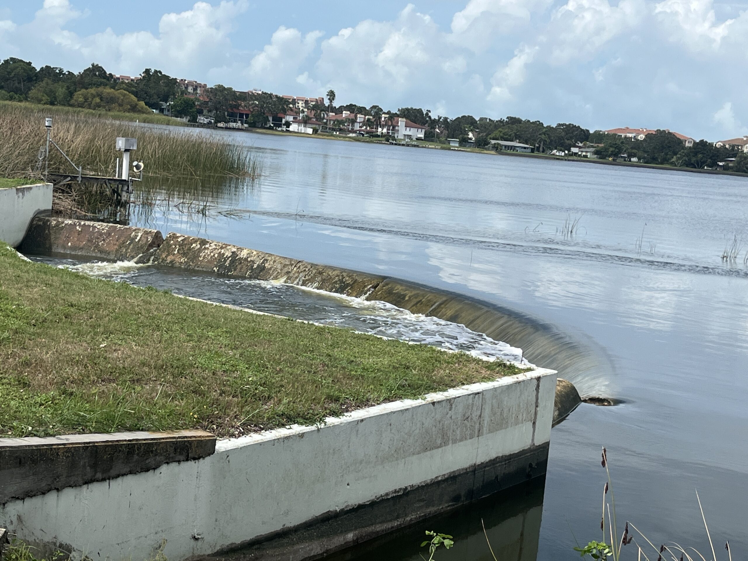 Man-made water channel with small waterfall and distant buildings across lake