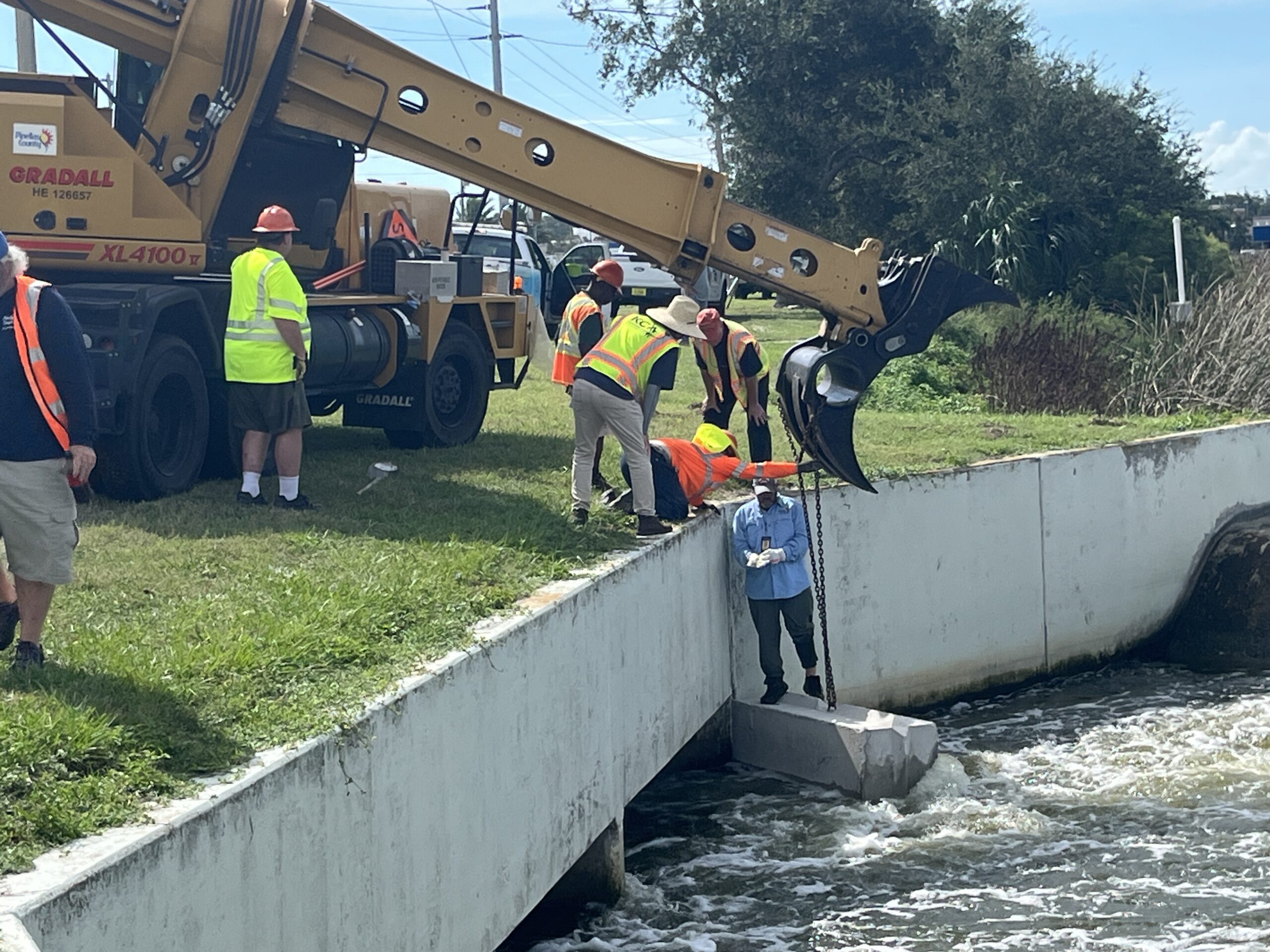 Construction workers using excavator by canal, adjusting concrete block