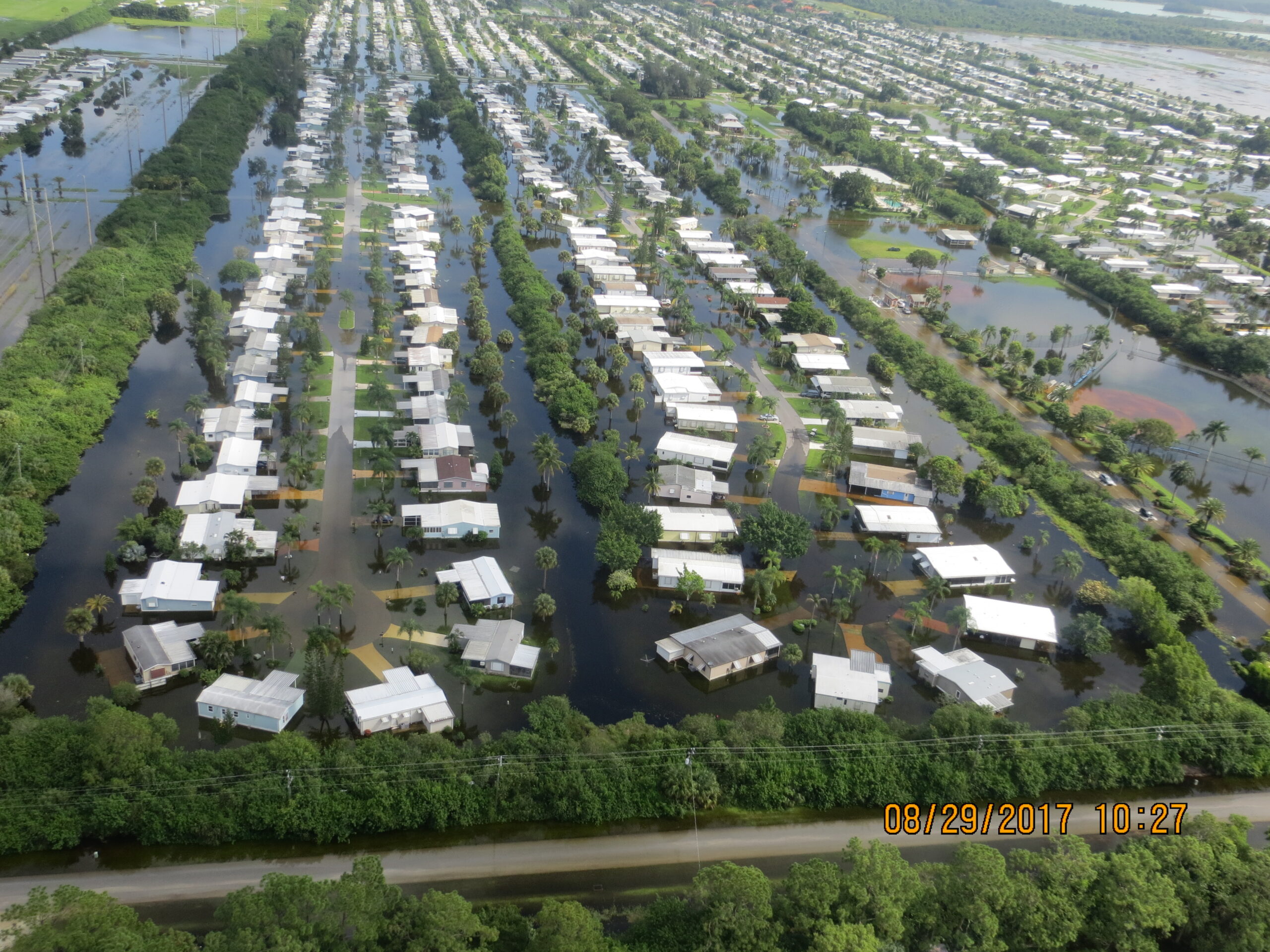 Aerial view of flooded residential area with date marked 08/29/2017 10:27. Houses are surrounded by water