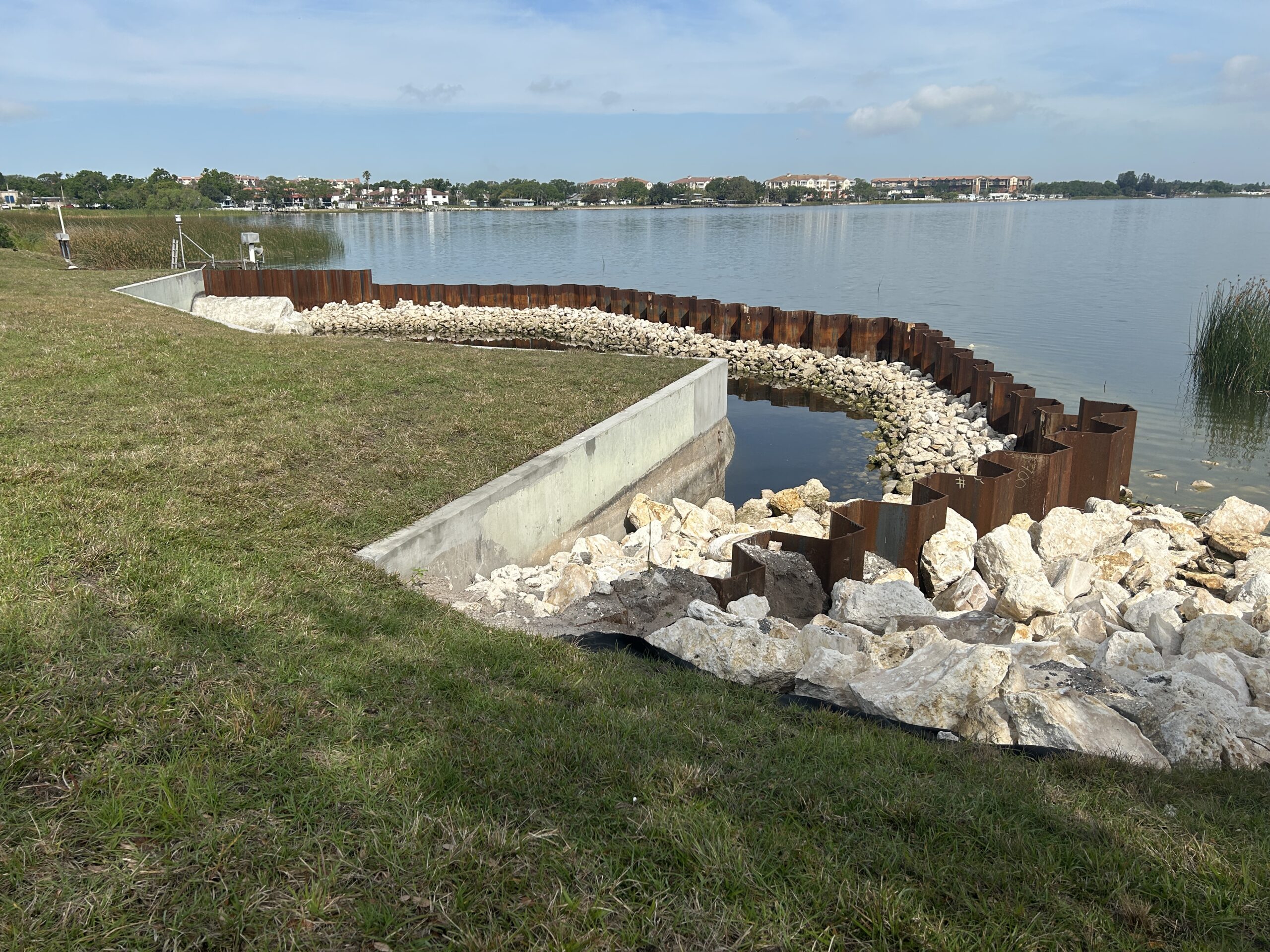 Rocky shoreline with rusted barriers along a calm lake under a blue sky
