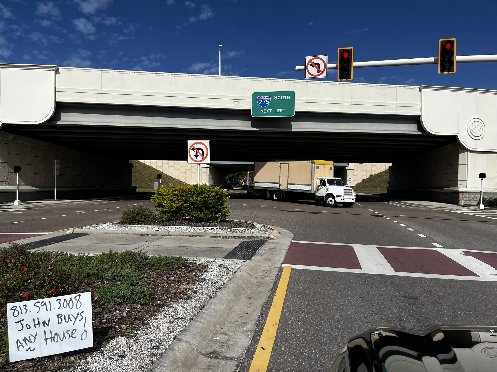 Truck under bridge, no left turn signs, and text: "813.591.3008 John Buys Any House."