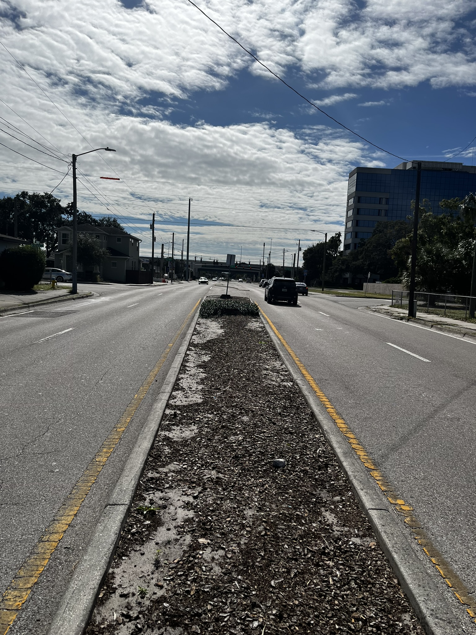 Empty road with cars, divided by central strip, under partly cloudy sky