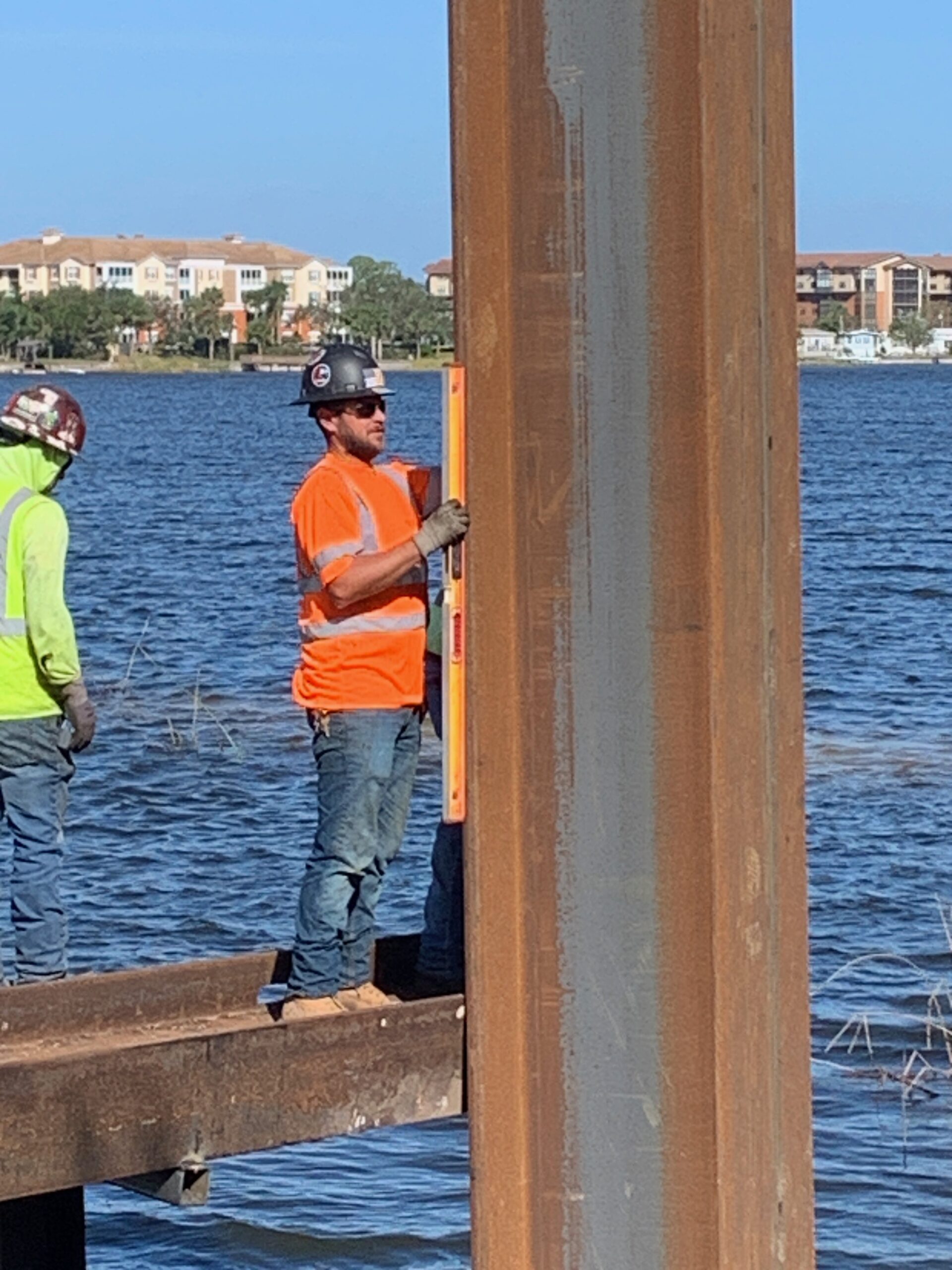 Worker in orange shirt using level on steel beam by water