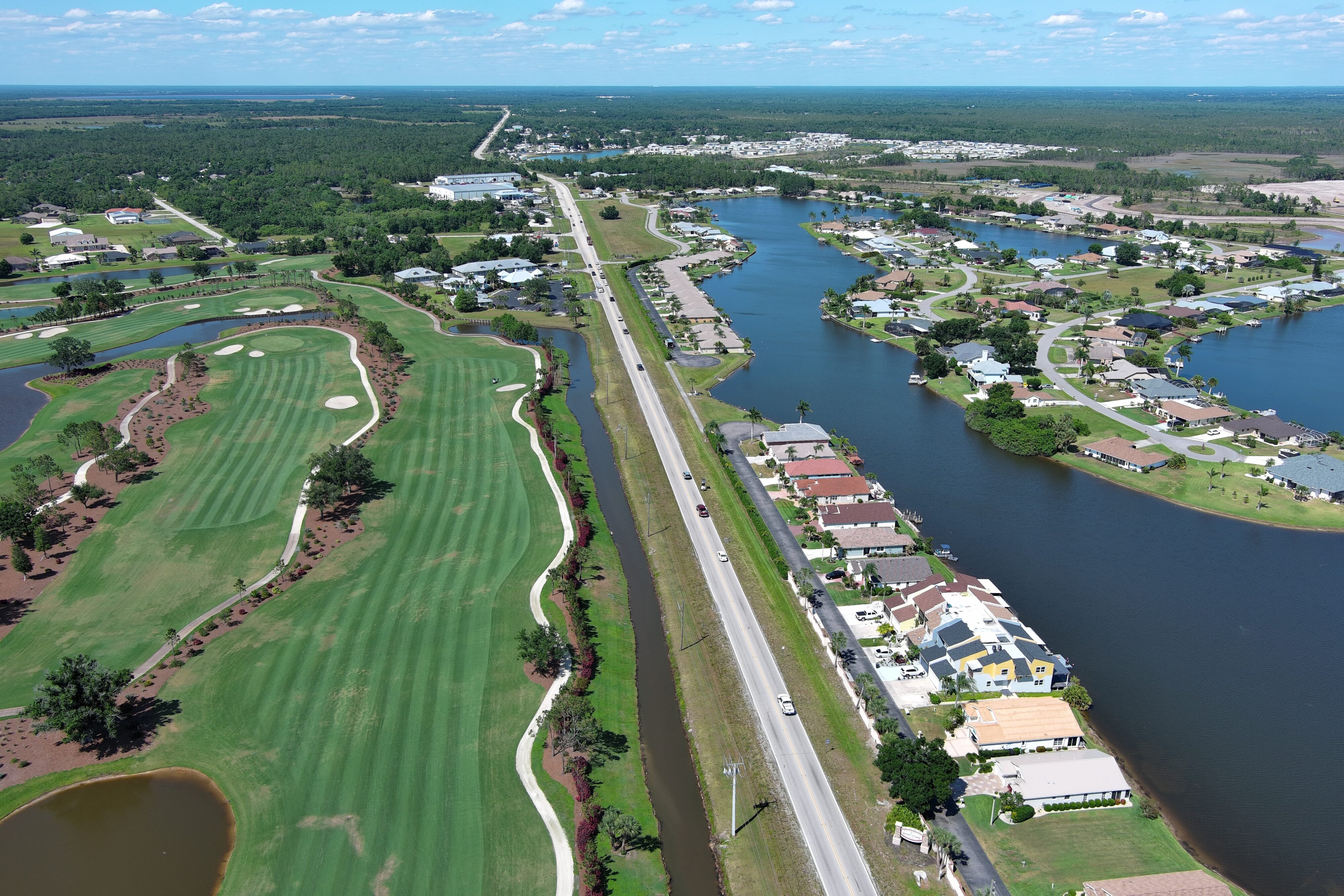 Aerial view of a golf course and residential neighborhood with surrounding water bodies