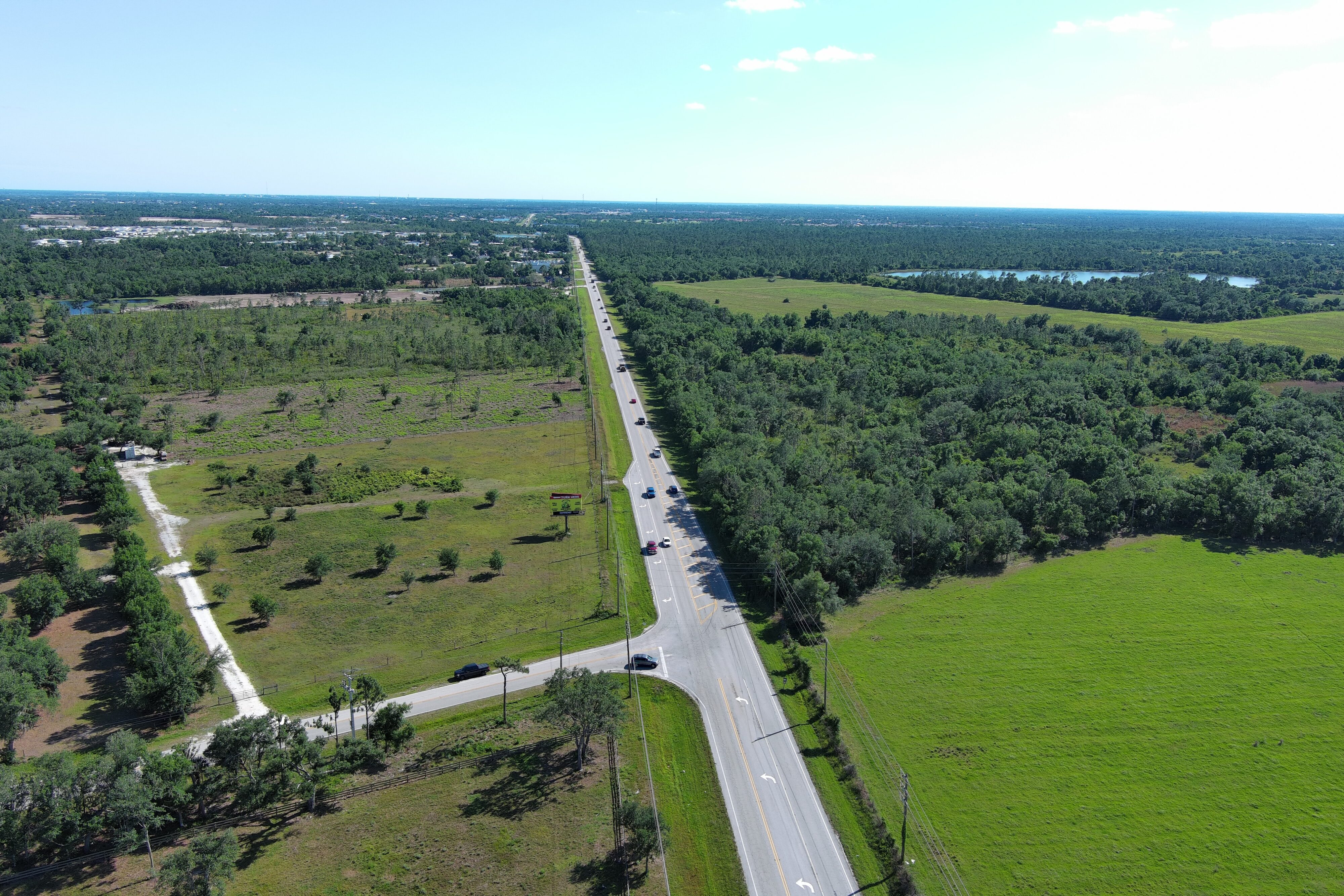 Aerial view of a long, straight highway surrounded by lush greenery and fields