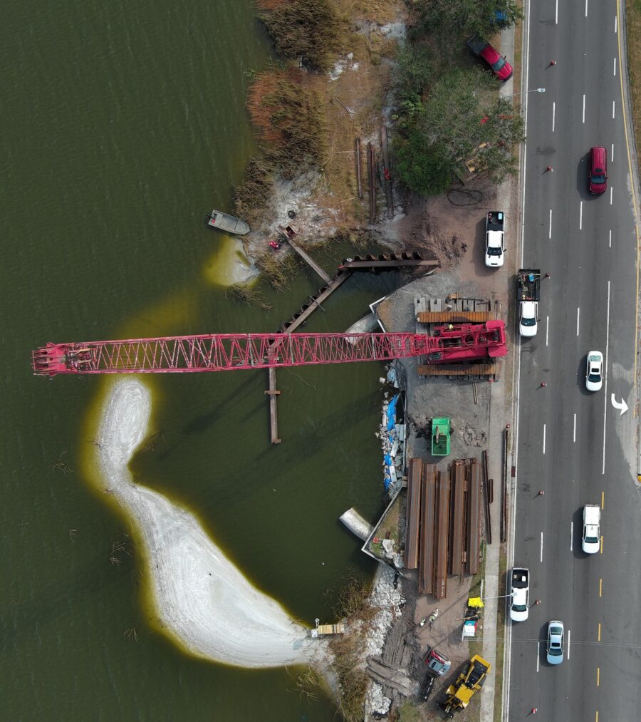 Aerial view of highway construction by a lake with a red crane