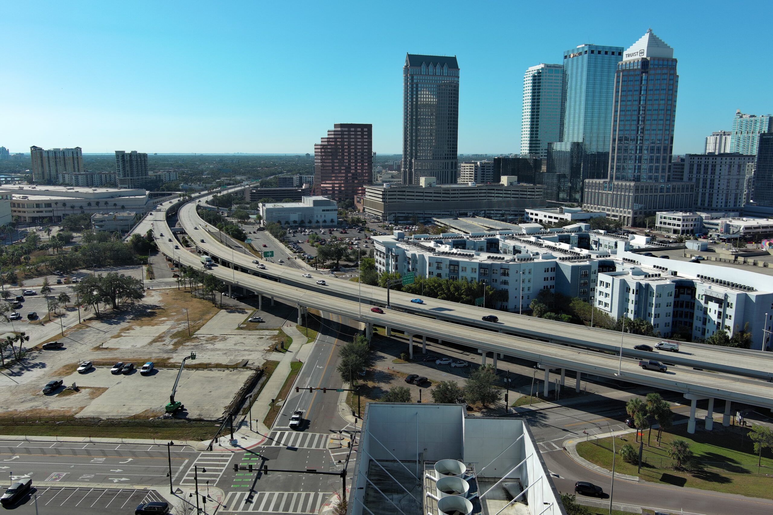 Aerial view of a cityscape with a highway, tall buildings, and a sunny sky
