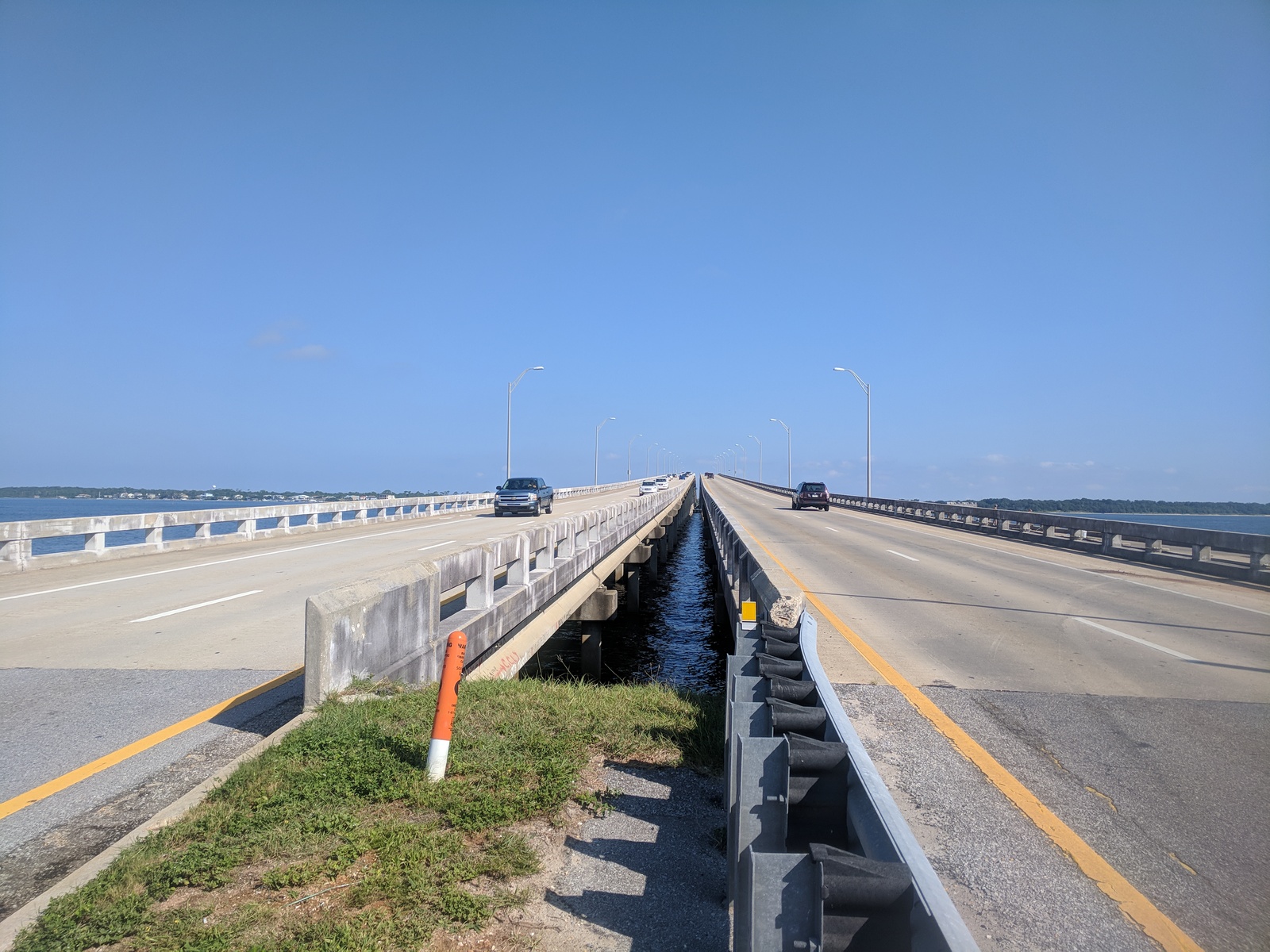 Two parallel bridges with vehicles, surrounded by water and sky