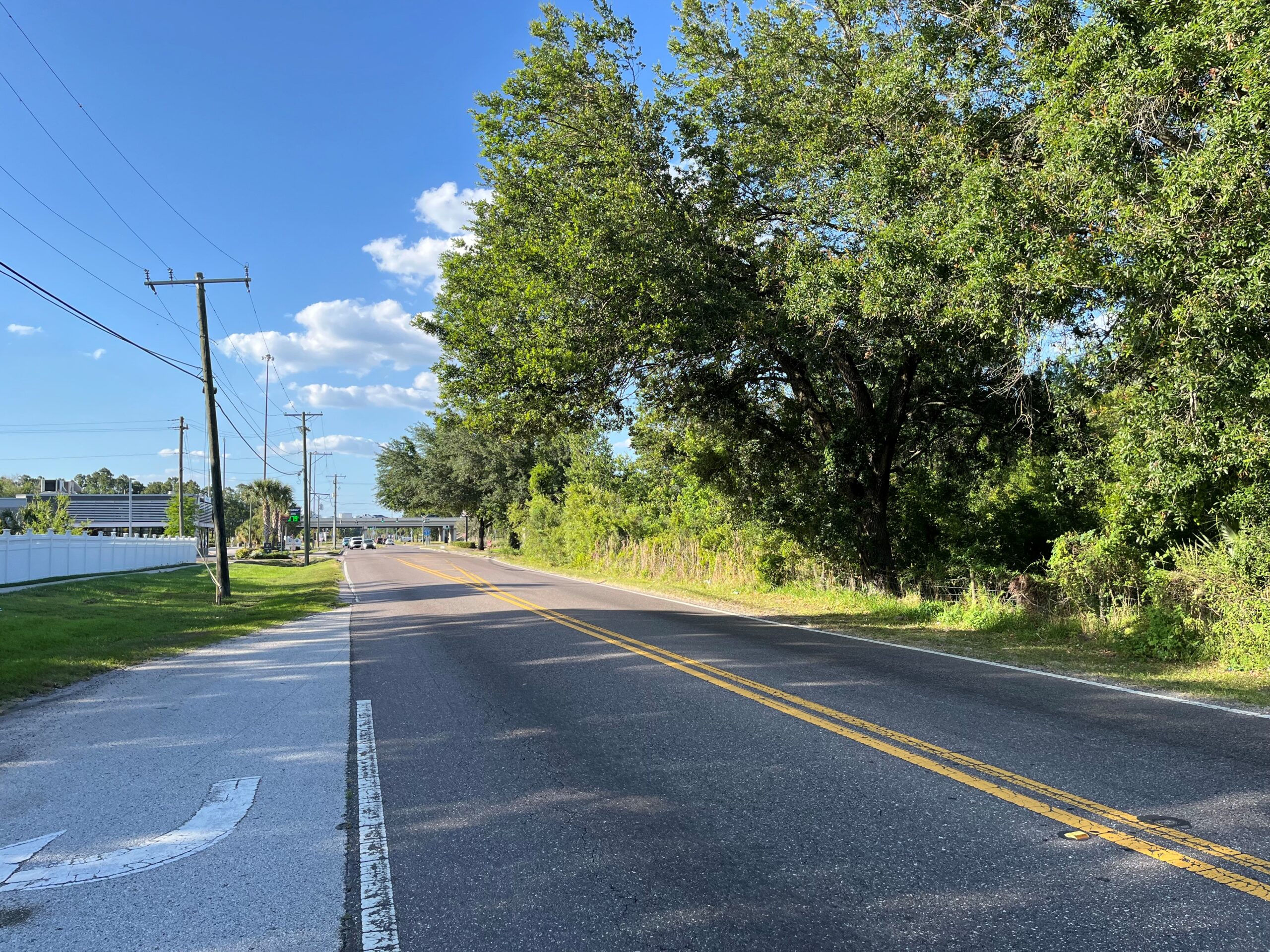 Rural road lined with trees and power lines under blue sky