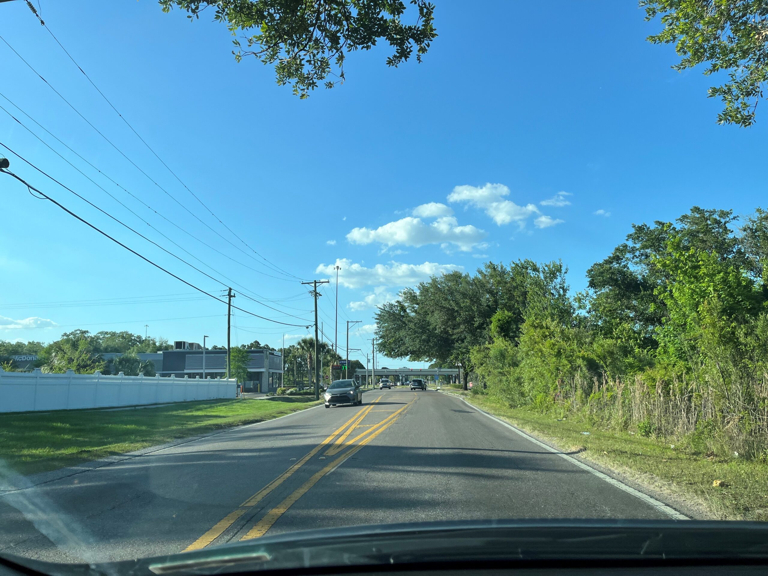 Driving on a suburban road with trees, power lines, and blue sky