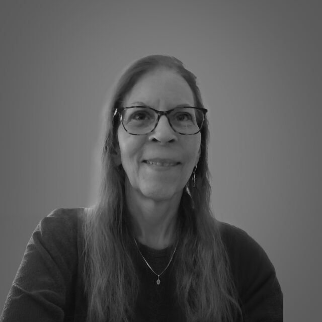 Miller smiling in black-and-white portrait, wearing glasses and necklace