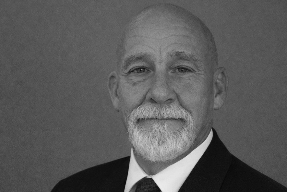 Patrick O'Grady in black and white portrait, wearing a suit, smiling subtly