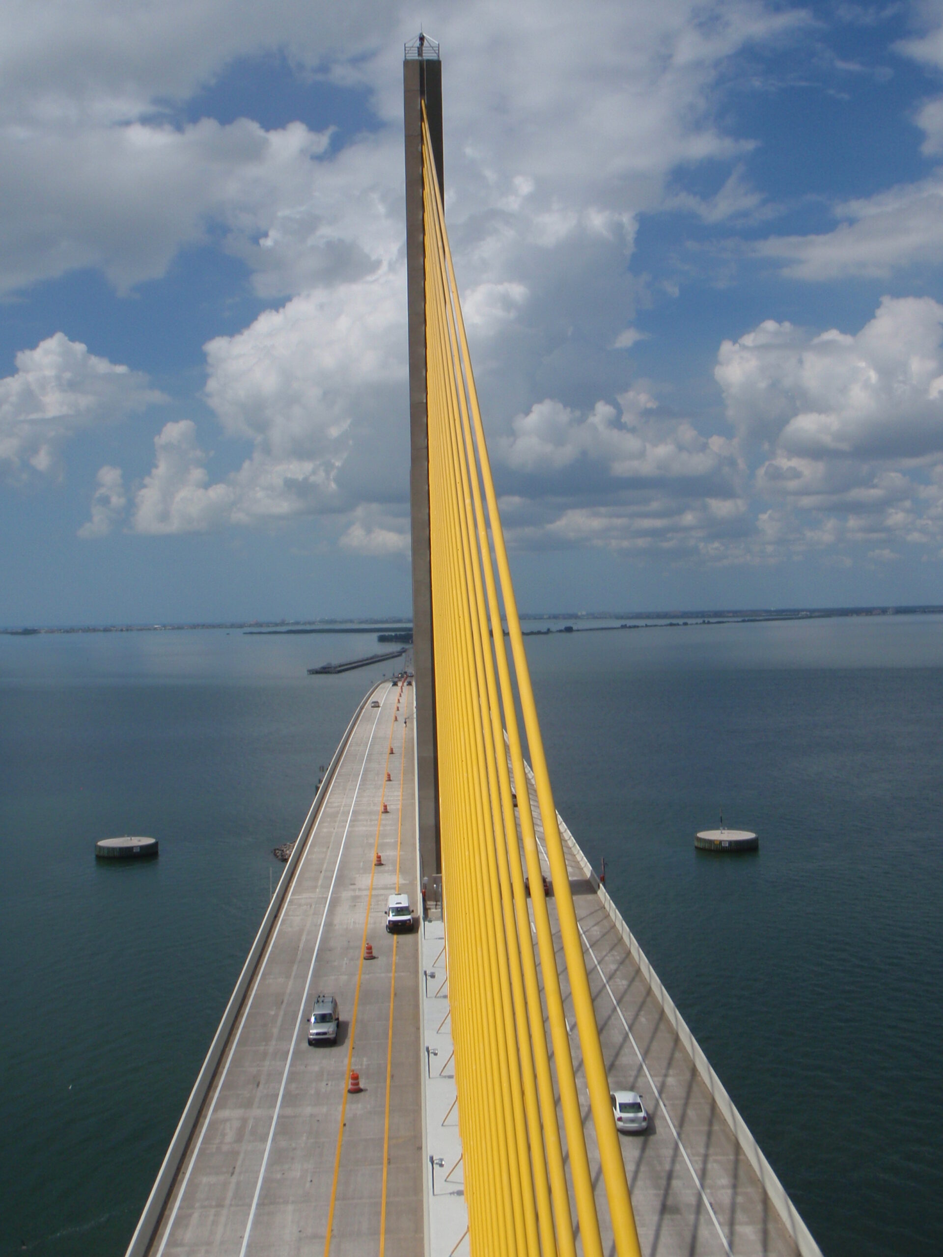 Yellow suspension bridge cables over calm water under a cloudy sky