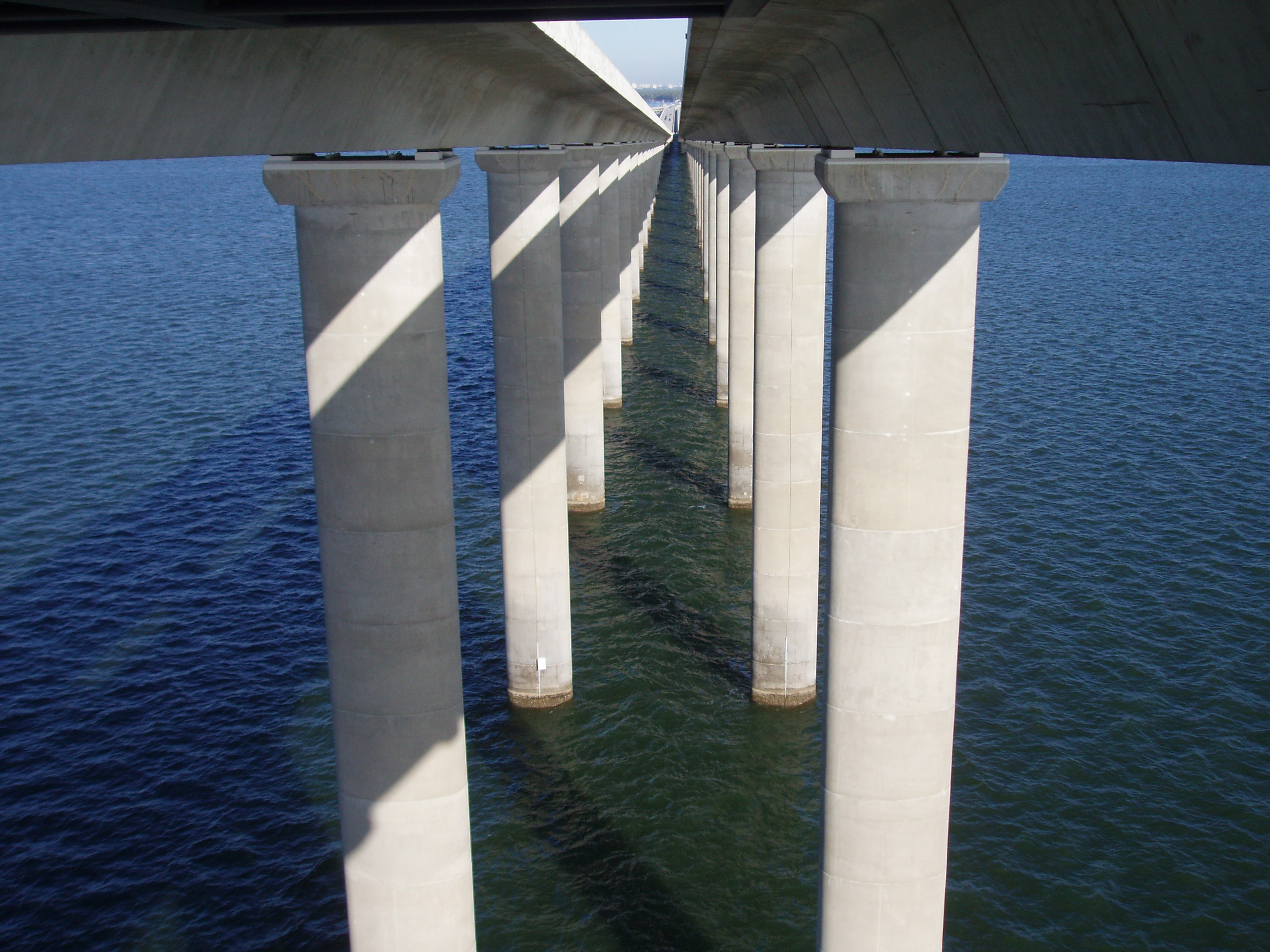 Concrete bridge columns over water, creating symmetry and shadow patterns