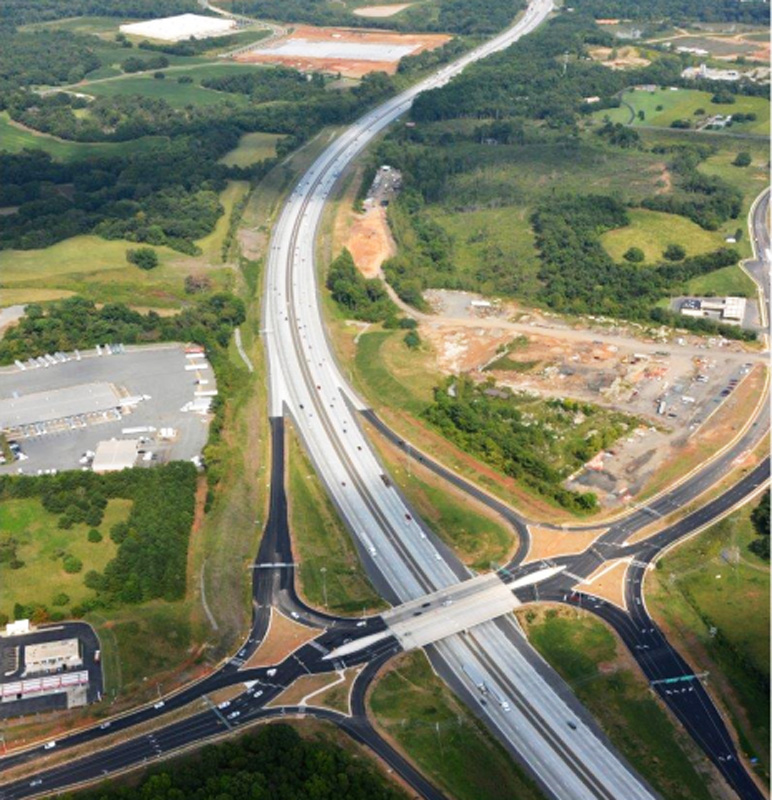 Aerial view of highway intersection on Poplar Tent Road over I-85, showcasing surrounding greenery and developments