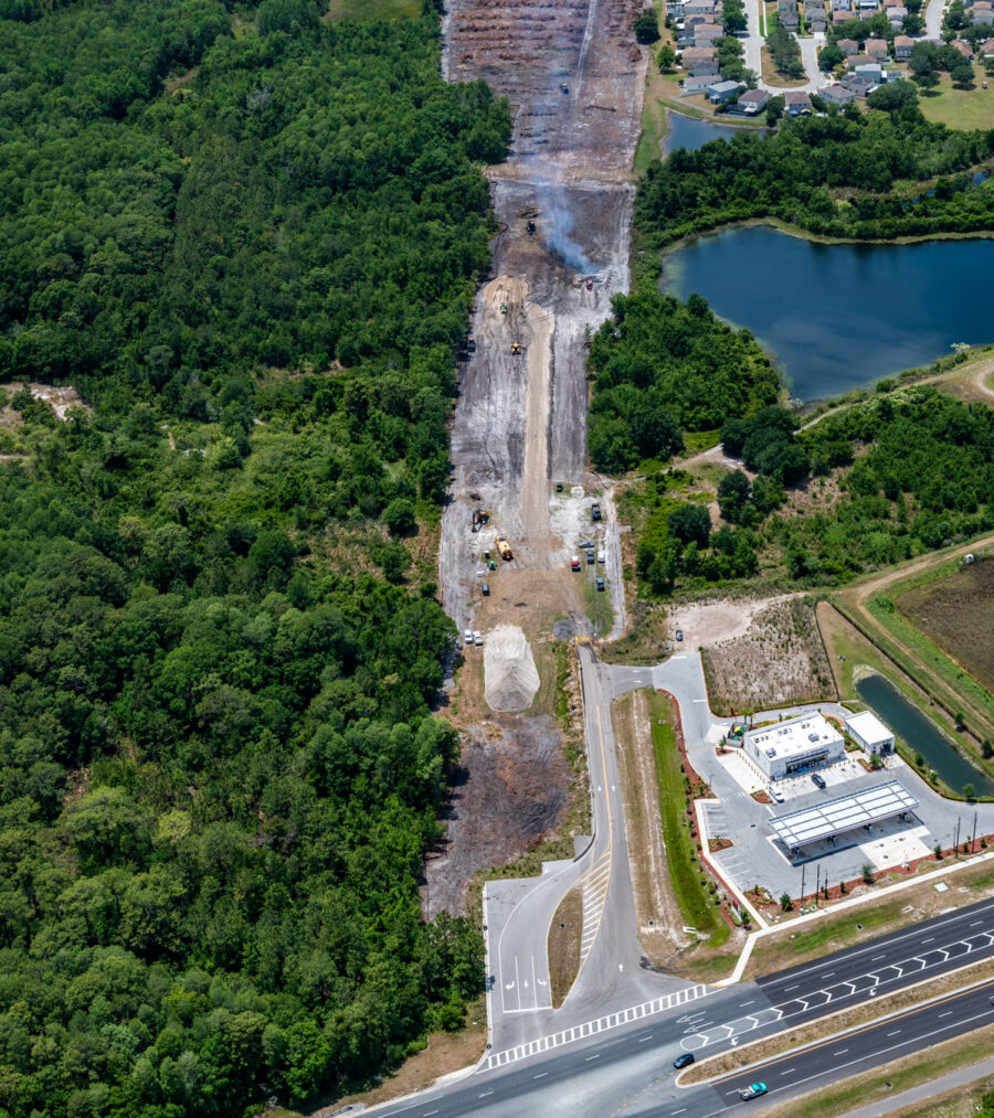 Aerial view of Ridge Road extension construction site surrounded by greenery, adjacent to a neighborhood and a pond