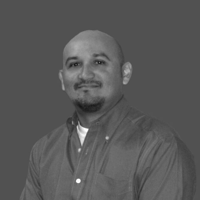 Antonio Rodriguez smiling, wearing a button-up shirt, grey background