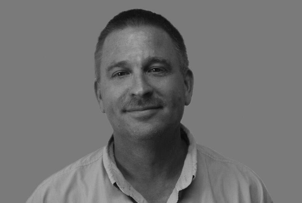 Rye John in black and white, smiling, wearing a collared shirt