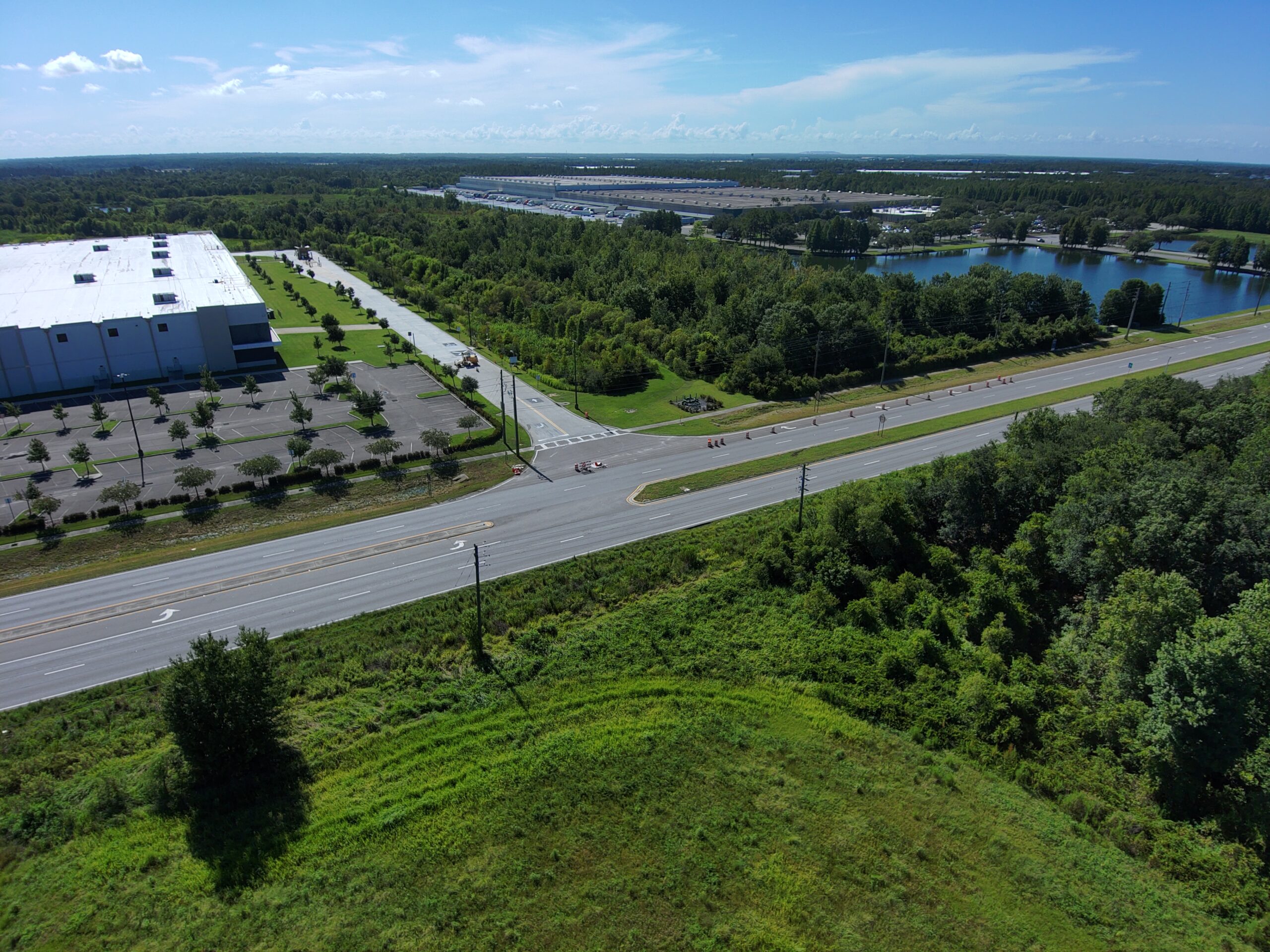 Warehouse adjacent to a road, with parking lot, trees, and water in background