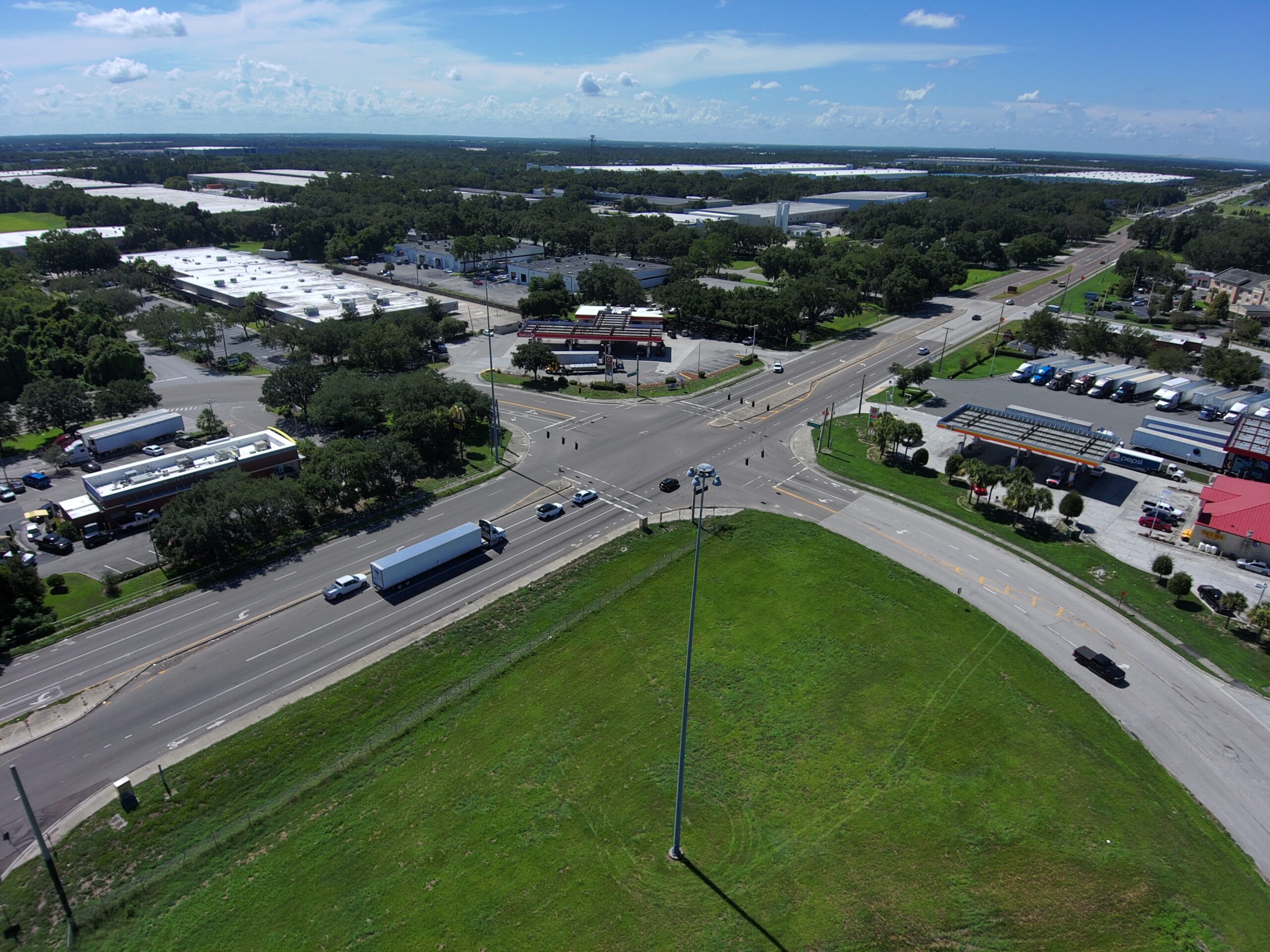 Aerial view of a busy intersection with surrounding commercial buildings and green areas under a clear blue sky