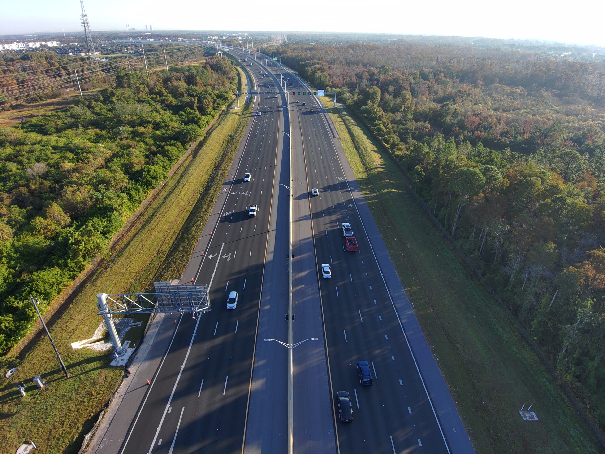Aerial view of a highway with sparse traffic surrounded by dense green foliage and power lines