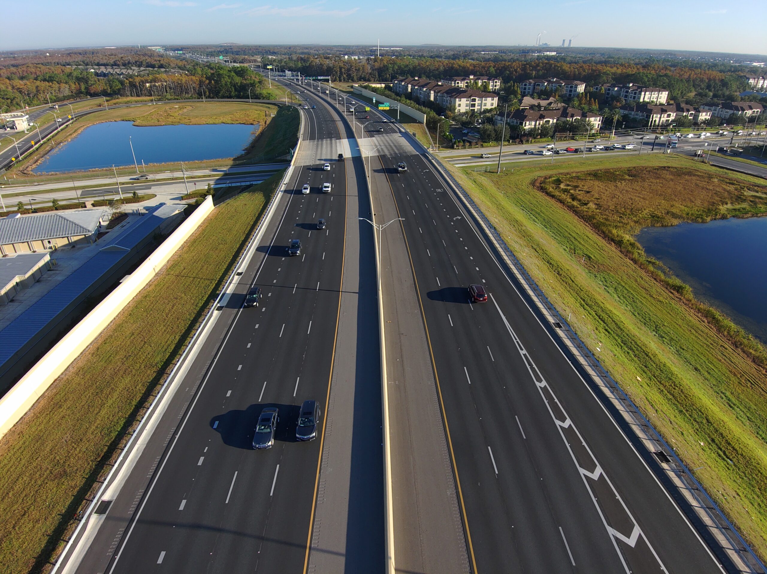 Aerial view of a multi-lane highway with sparse traffic, surrounded by green fields and ponds