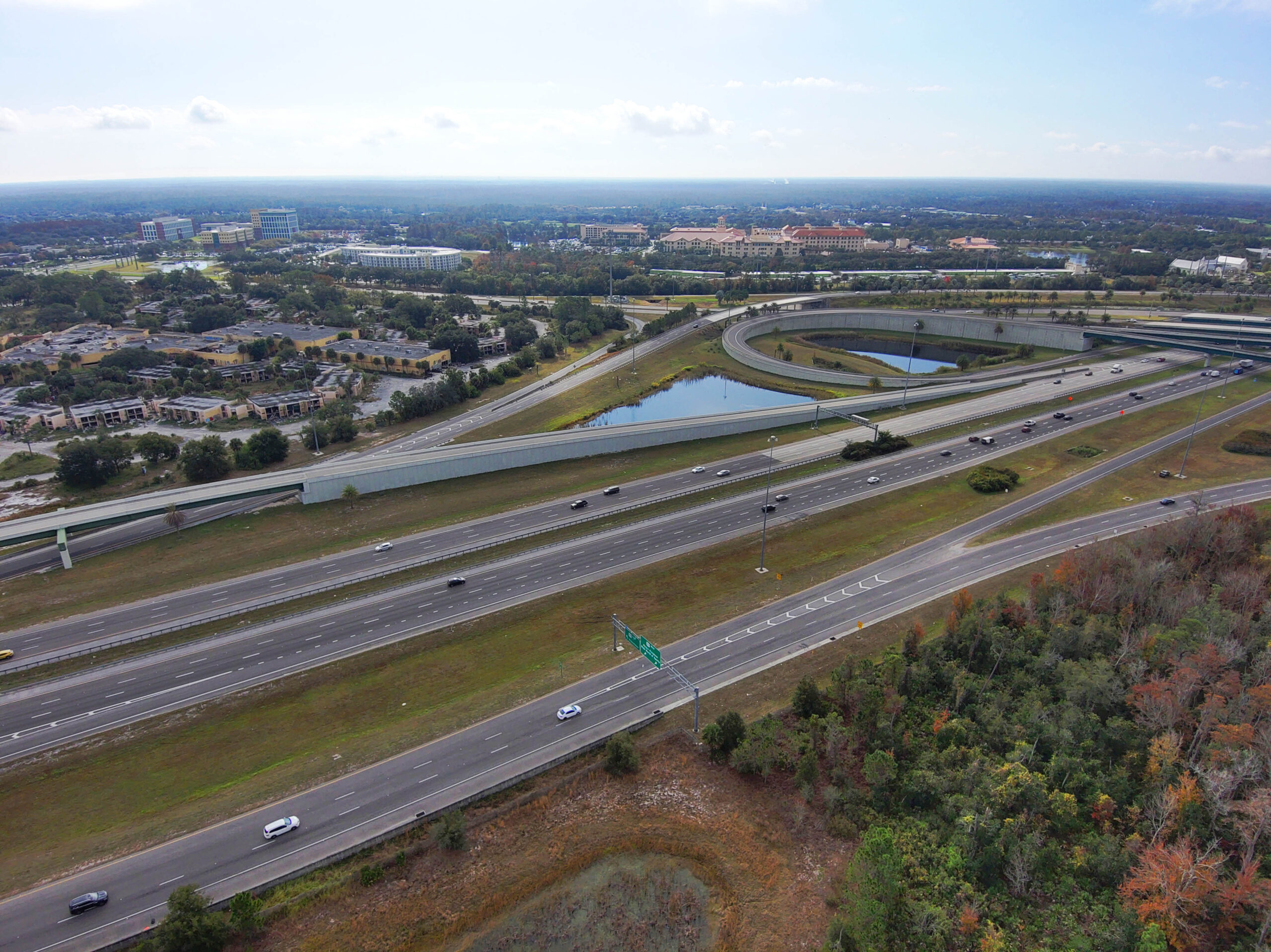 Aerial view of a highway interchange surrounded by greenery and city buildings in the background