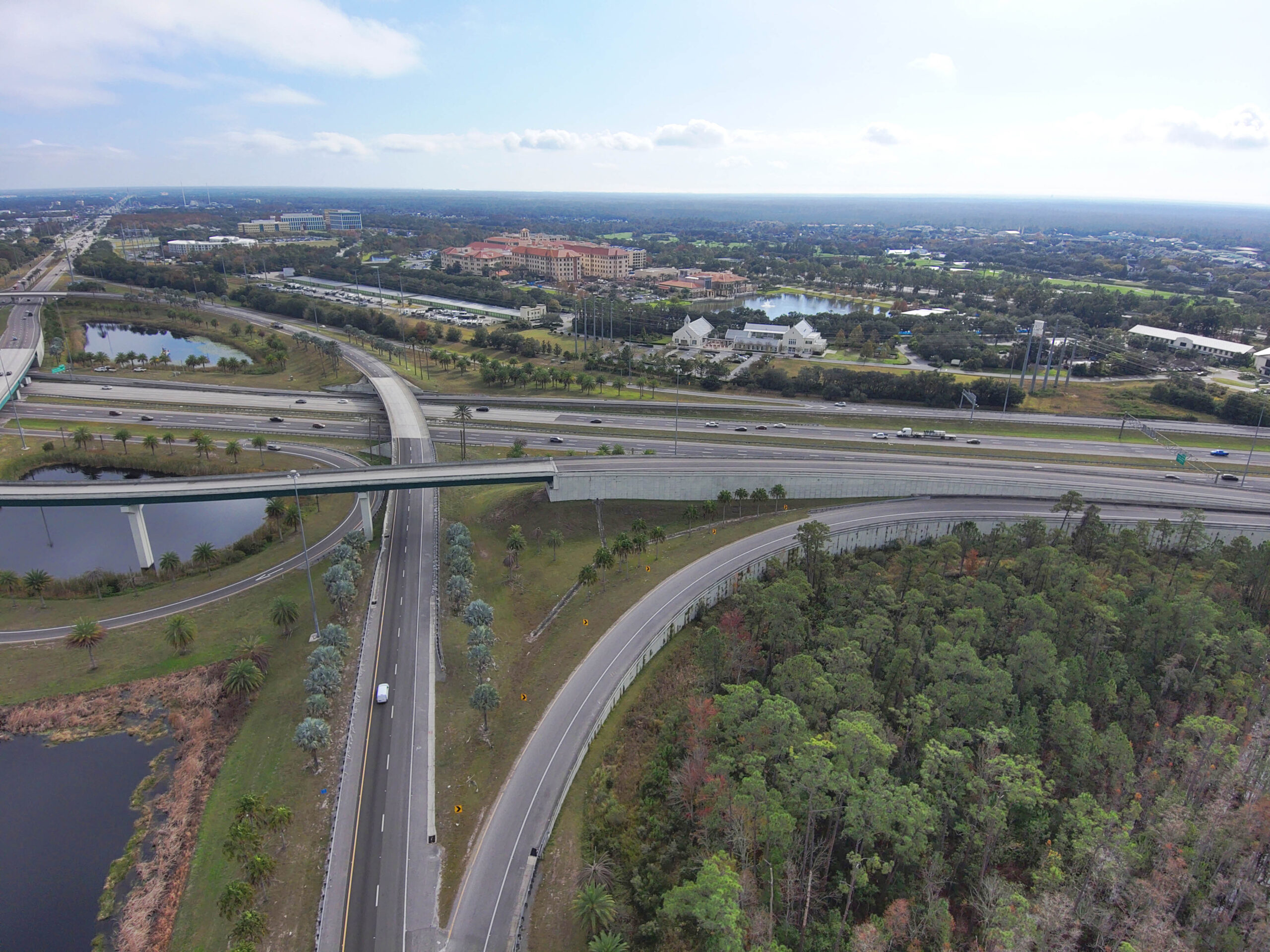 Aerial view of a highway interchange with surrounding greenery and buildings in the distance
