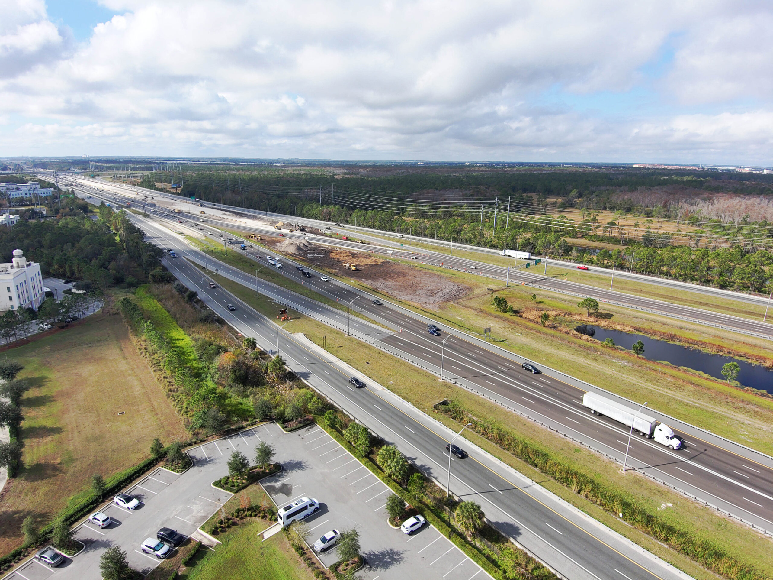 Highway with moderate traffic, surrounded by greenery, under partly cloudy sky